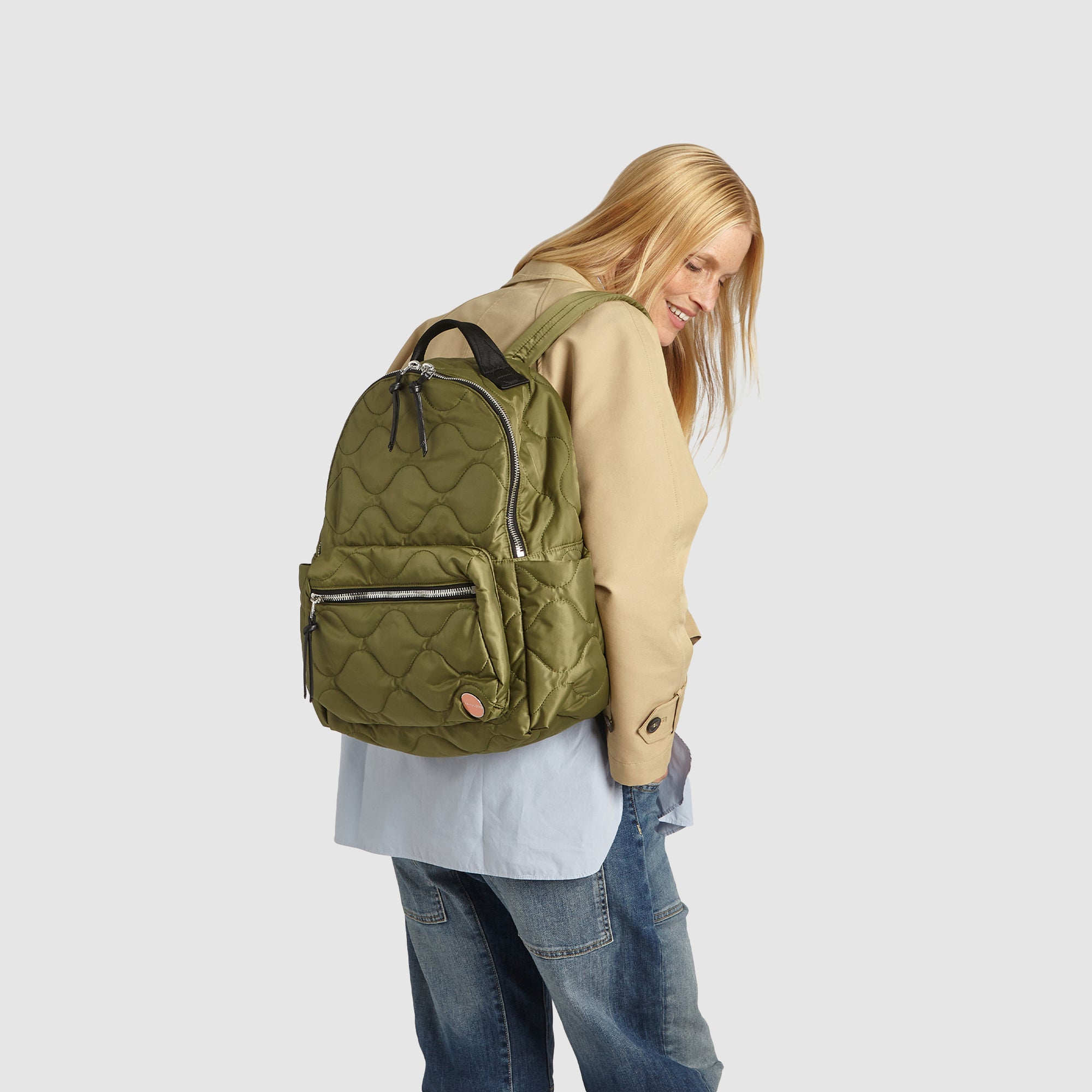 Person wearing a sage green quilted tate backpack on a plain background