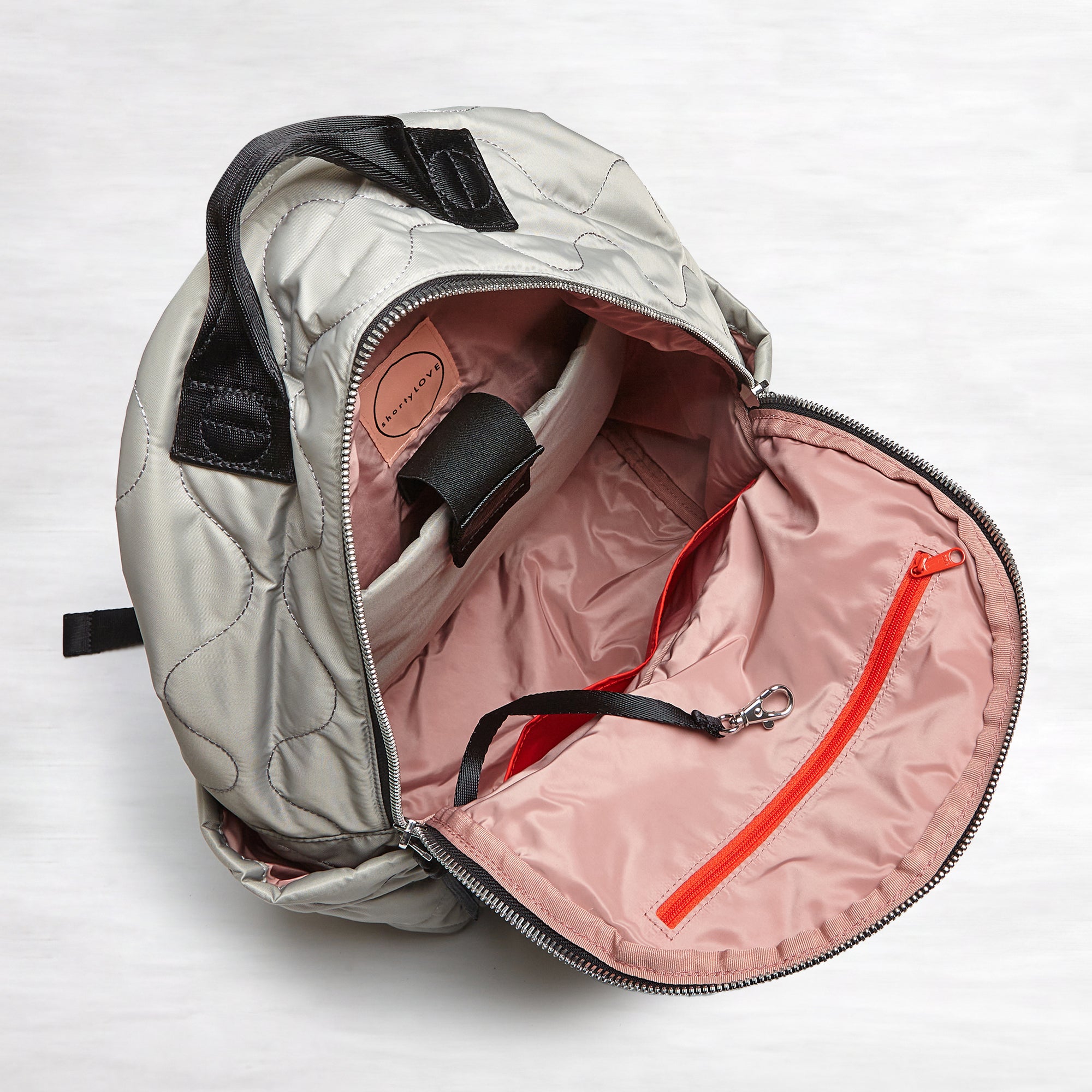 shortyLOVE tate backpack in milky grey; top-down view showing interior blush lining against white background.