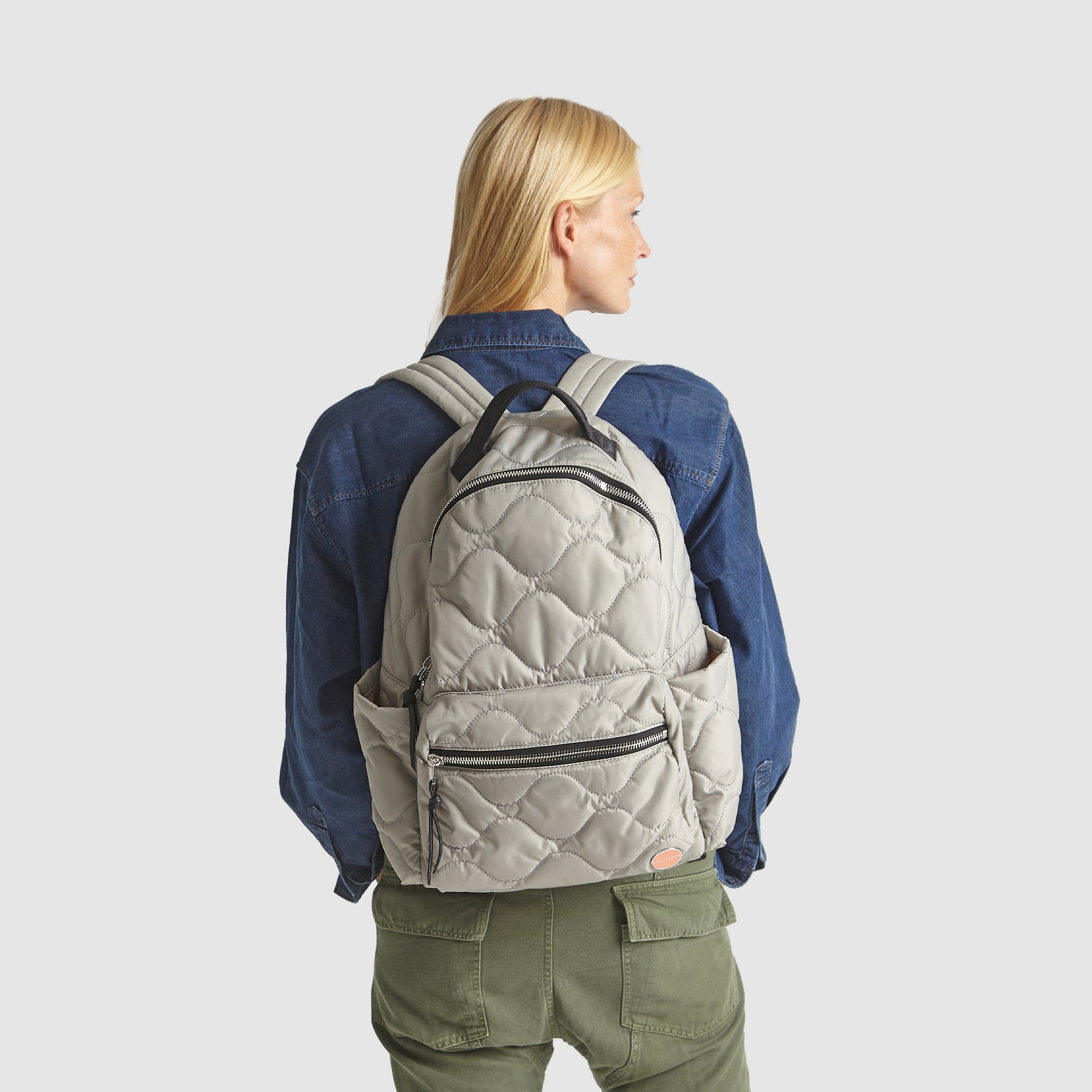 Person wearing a gray quilted tate backpack on a plain background