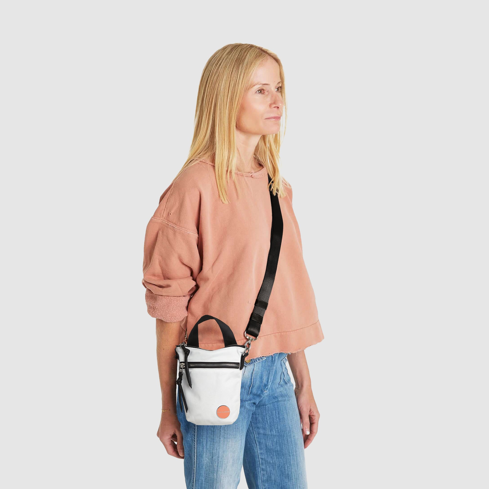 shortyLOVE shorthand small crossbody bag in white; on model in peach sweatshirt and jeans against white background.