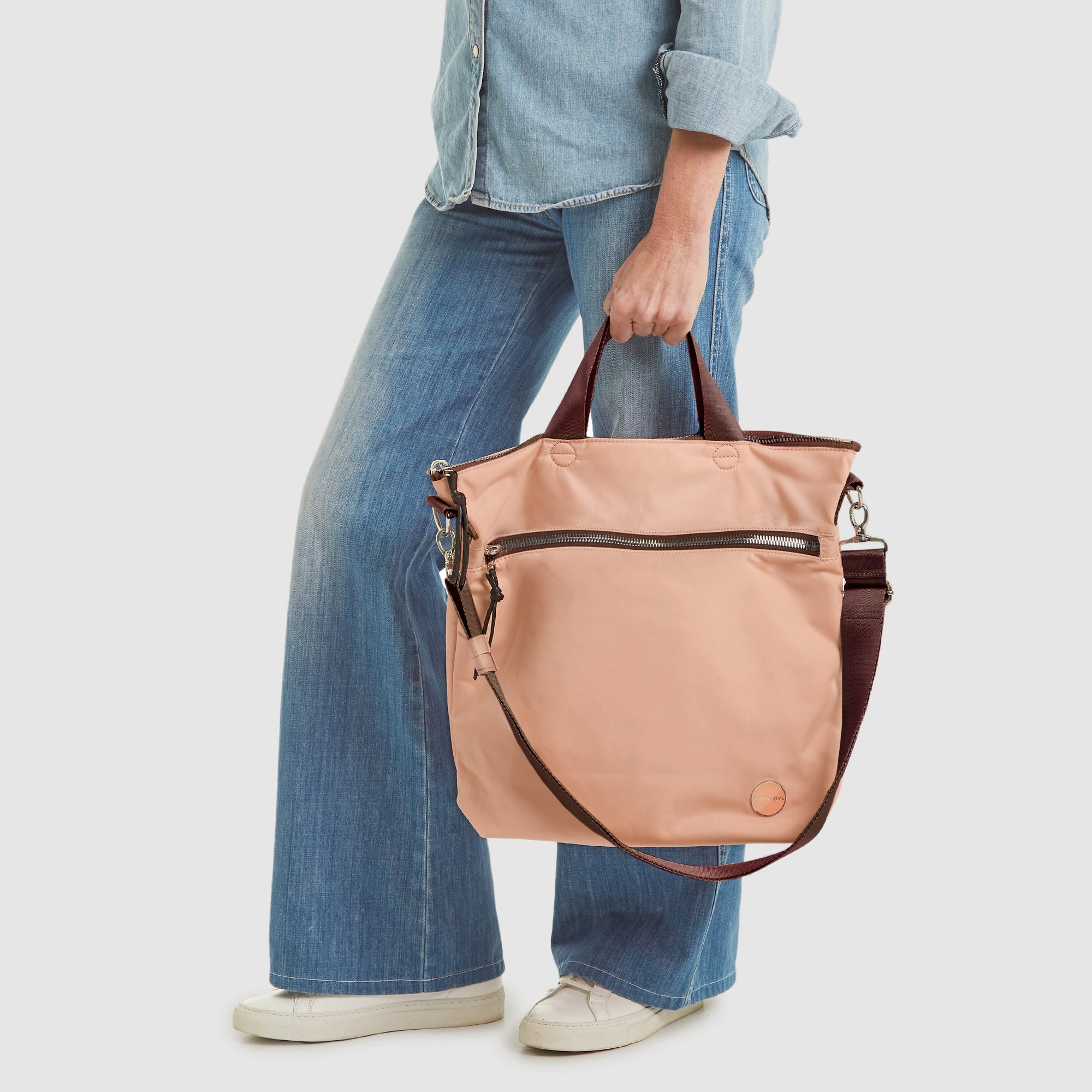 shortyLOVE wonder large crossbody/messenger bag in dusty peach; hand held by model in jeans against white background.