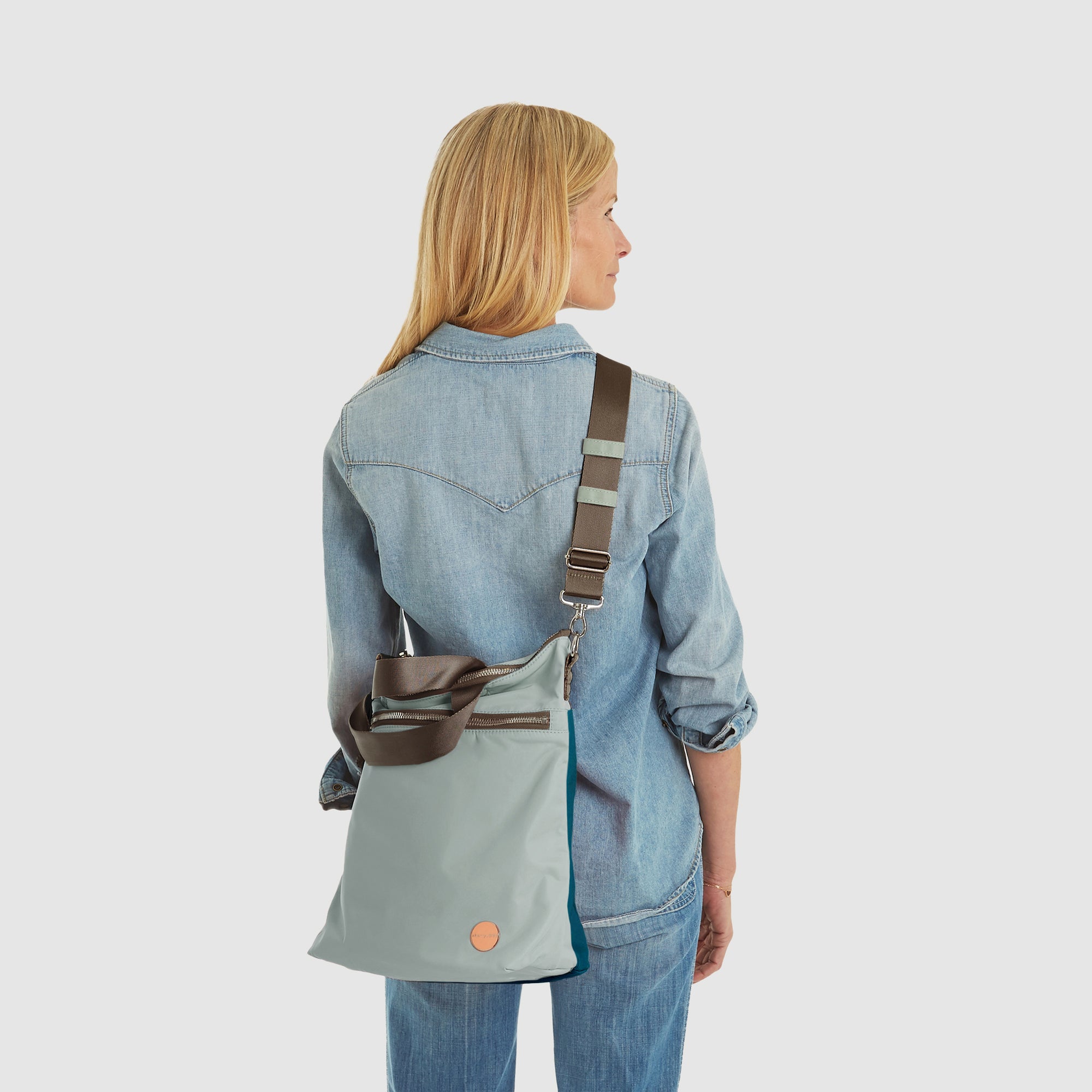 shortyLOVE wonder large crossbody/messenger bag in slate/teal; on model in jean shirt and jeans against white background.