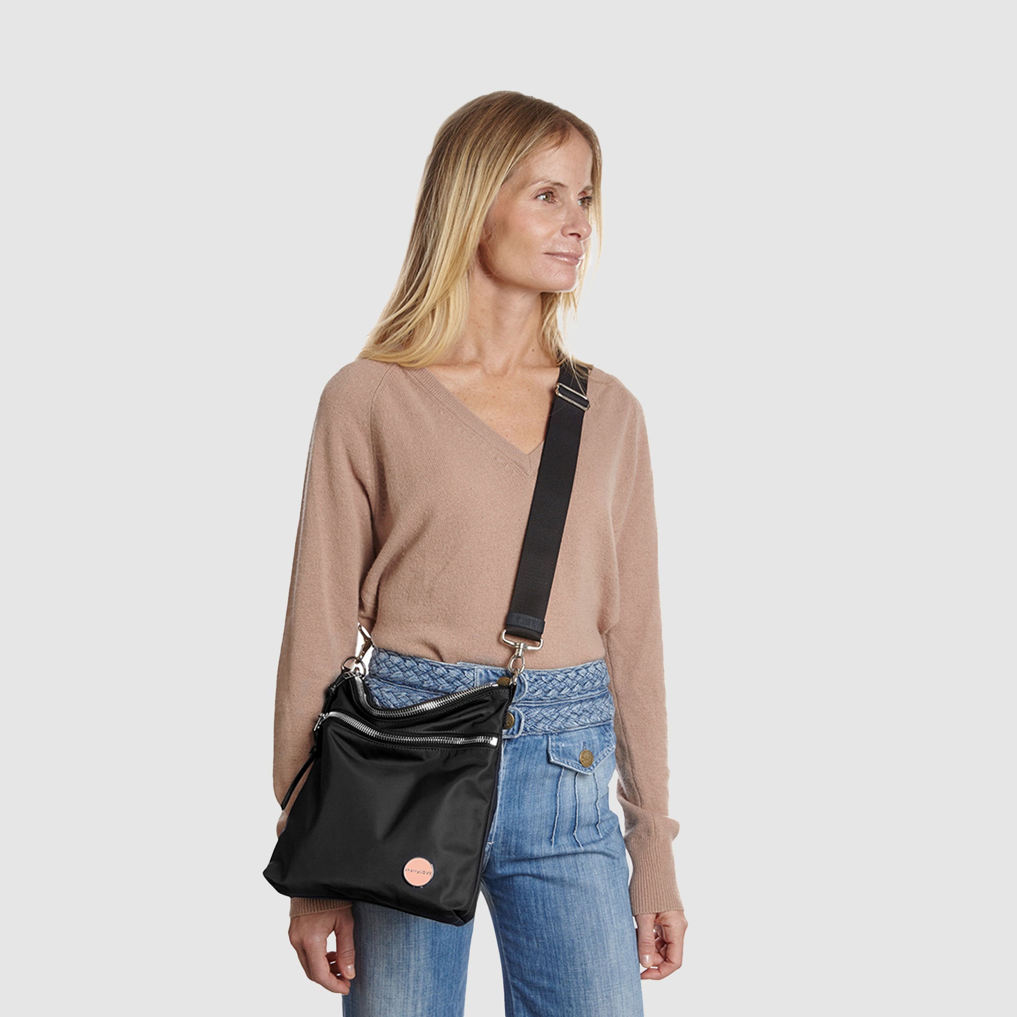 shortyLOVE amuse medium sized crossbody bag in black; on model in tan v-neck long sleeve sweater and jeans against white background.