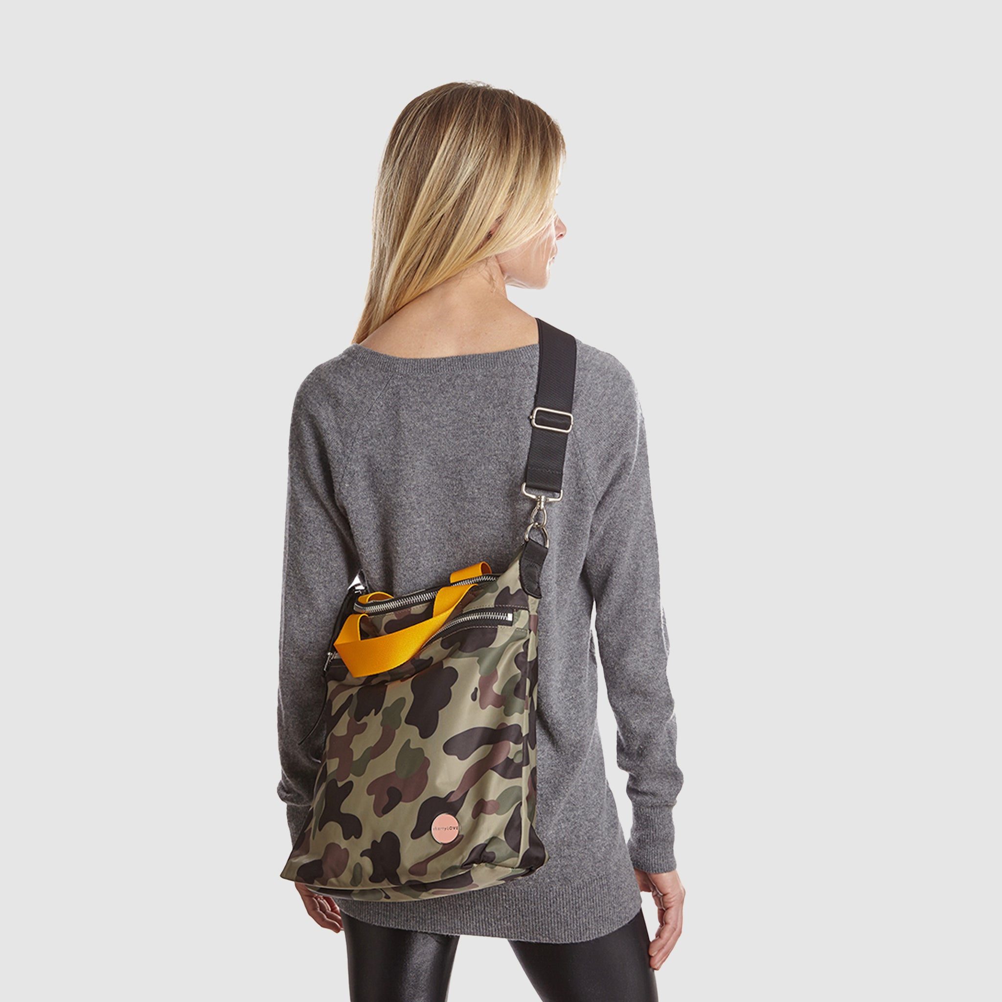 shortyLOVE wonder large crossbody/messenger bag in green camo; worn crossbody by model in grey long sleeve sweater and black leggings against white background.