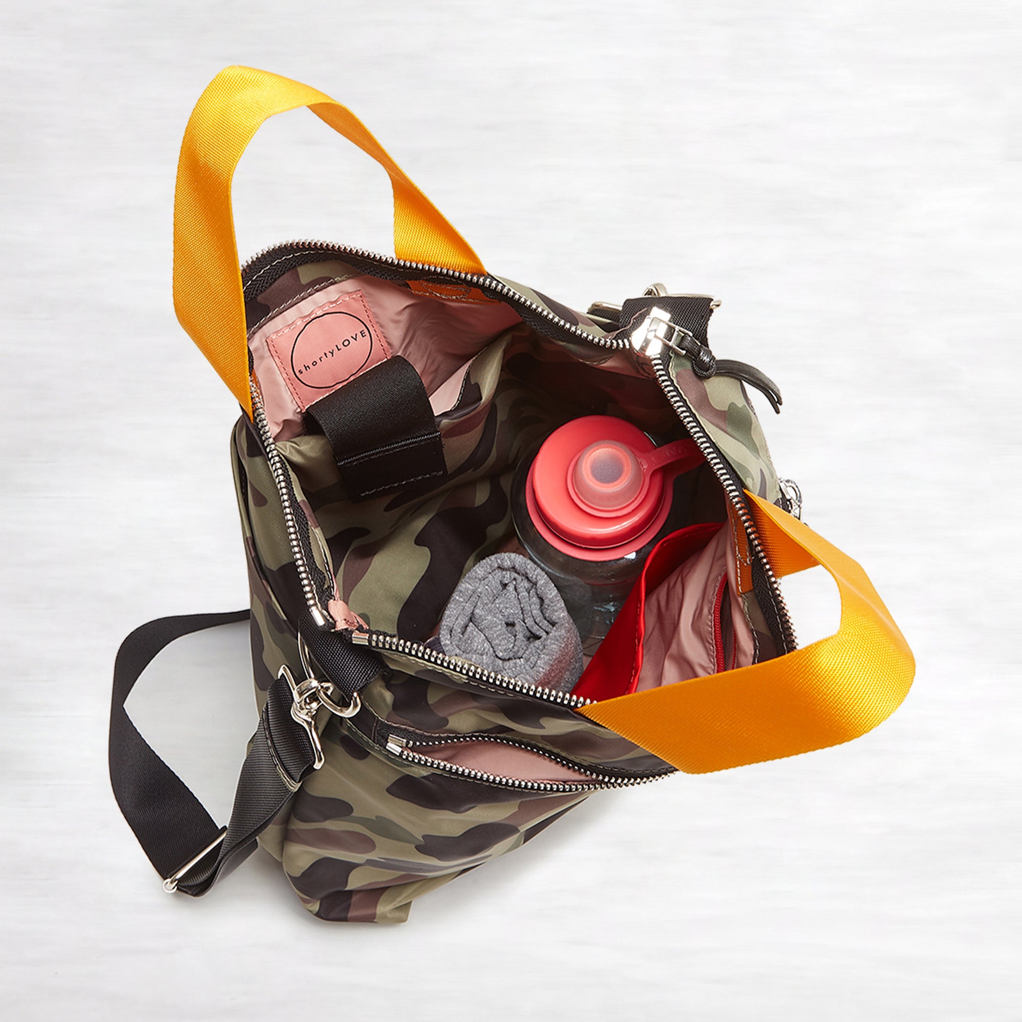 shortyLOVE wonder large crossbody/messenger bag in green camo; top-down view showing interior pink lining against white background.