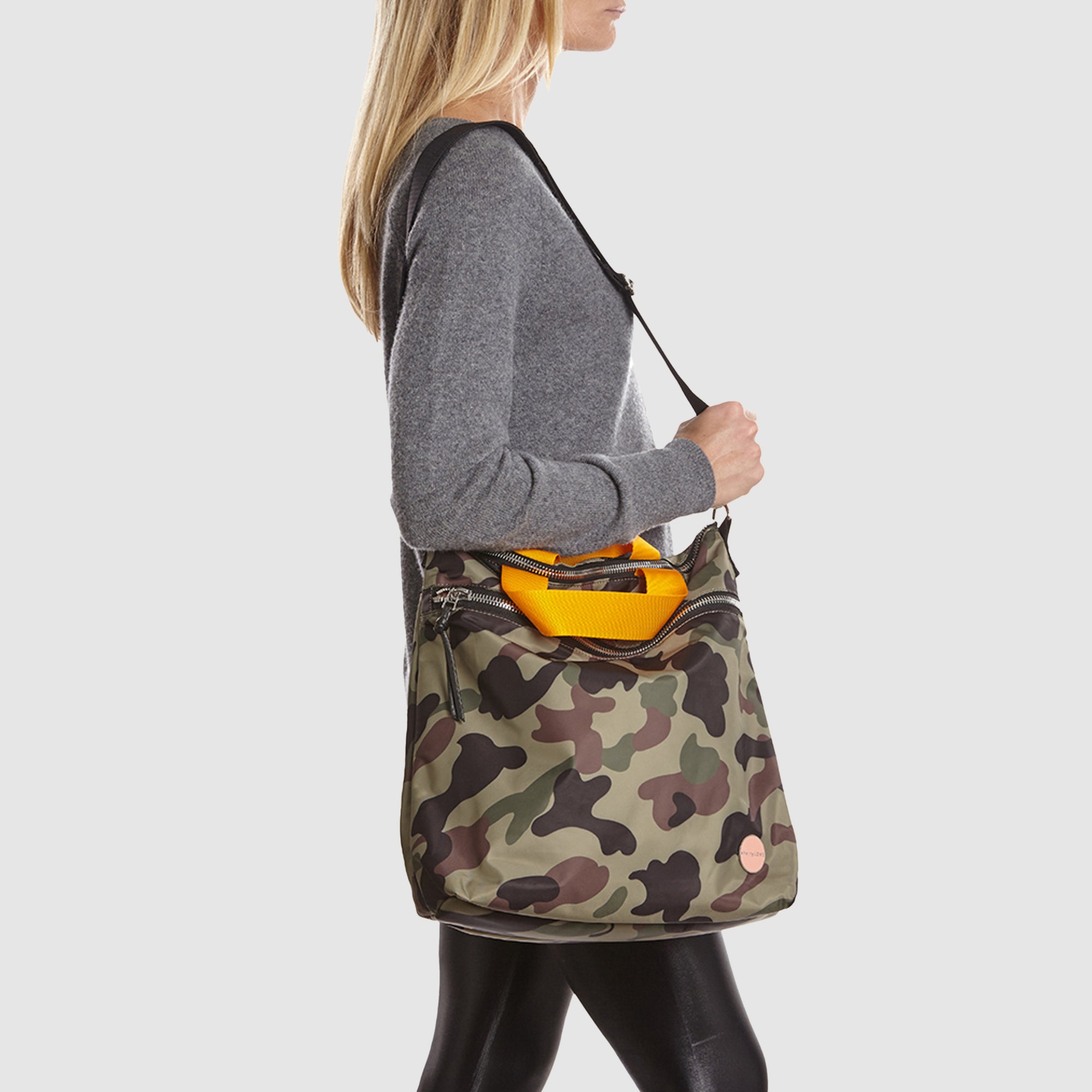 shortyLOVE wonder large crossbody/messenger bag in green camo; worn crossbody by model in grey long sleeve sweater and black leggings against white background.