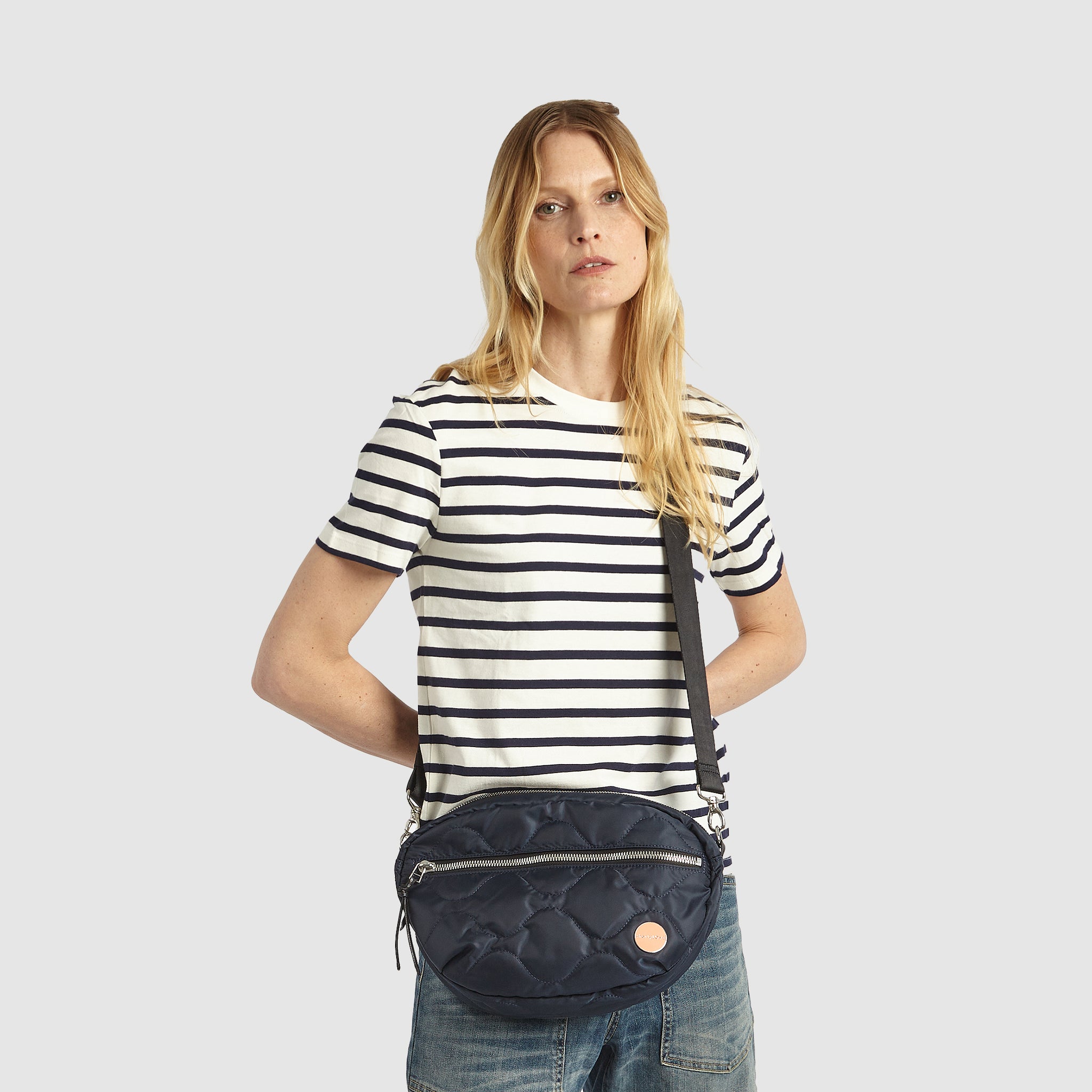 shortyLOVE cruiser medium crossbody bag in midnight; on model in striped blue and white shirt and jeans against white background.