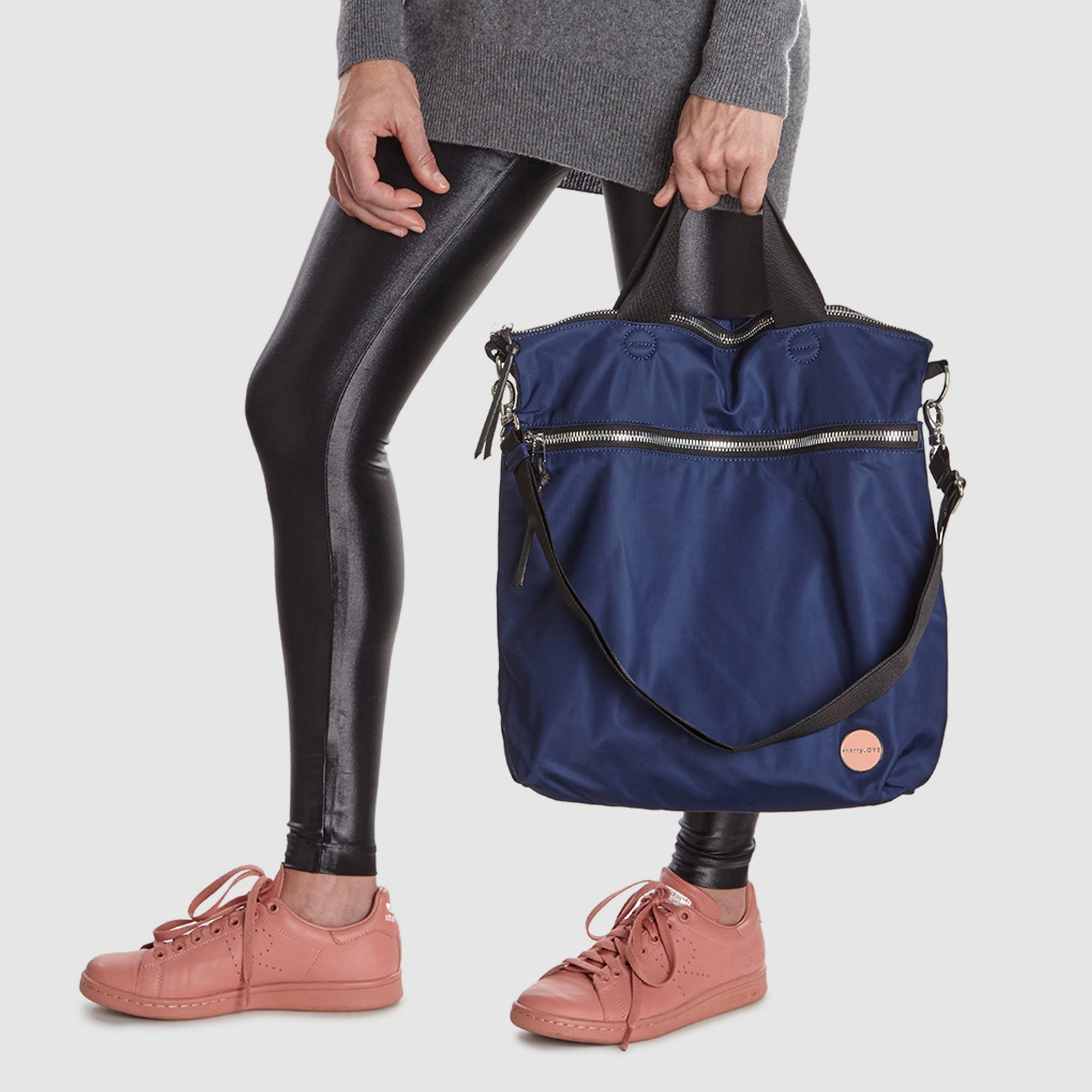 shortyLOVE wonder large crossbody/messenger bag in navy; hand held by model in grey long sleeve sweater and black leggings against white background.