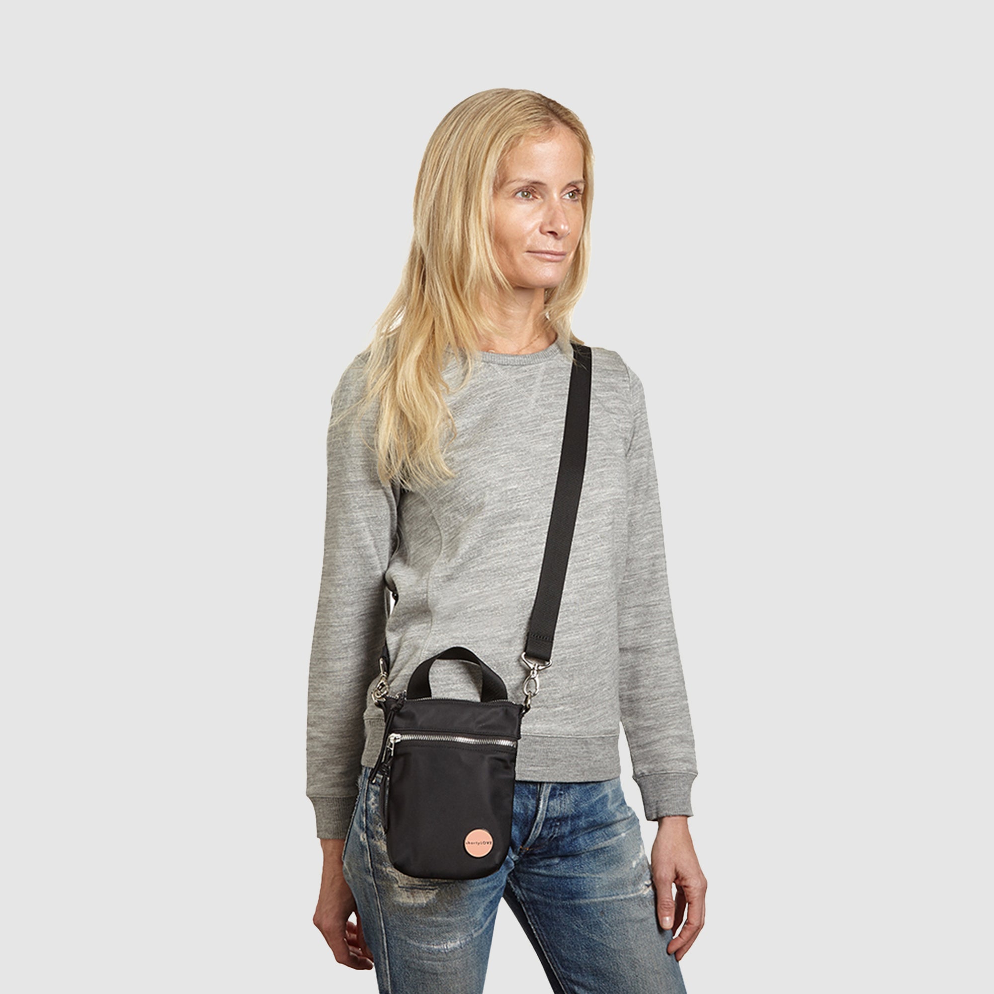 shortyLOVE shorthand crossbody phone bag in black; on model in grey sweatshirt and jeans against white background