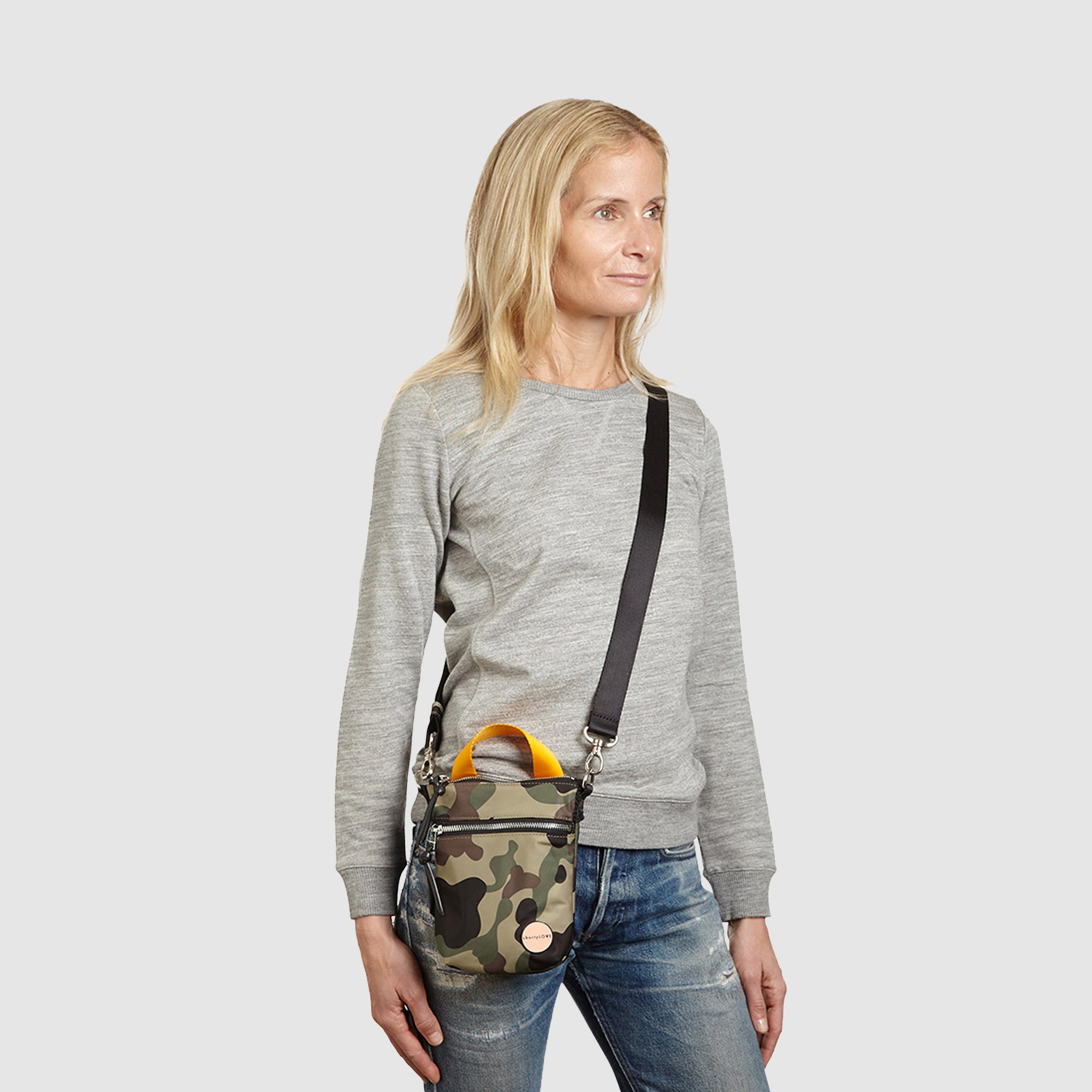 shortyLOVE shorthand crossbody phone bag in green camo; on model in grey sweatshirt and jeans against white background