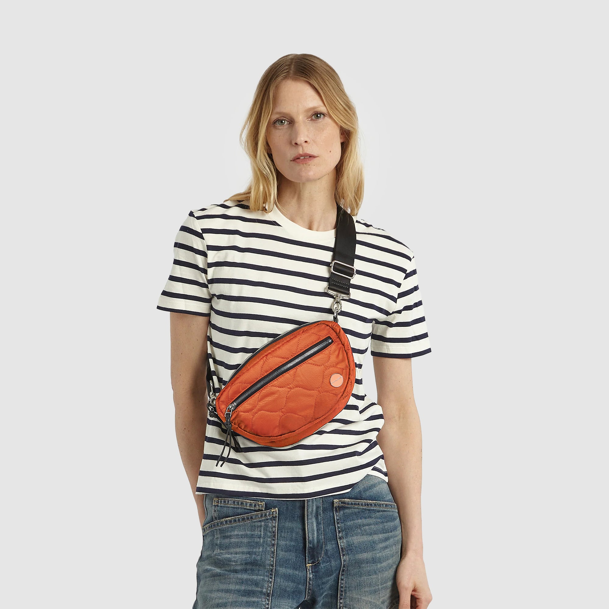 Model in striped tee short and jeans wearing an orange small cruiser crossbody bag