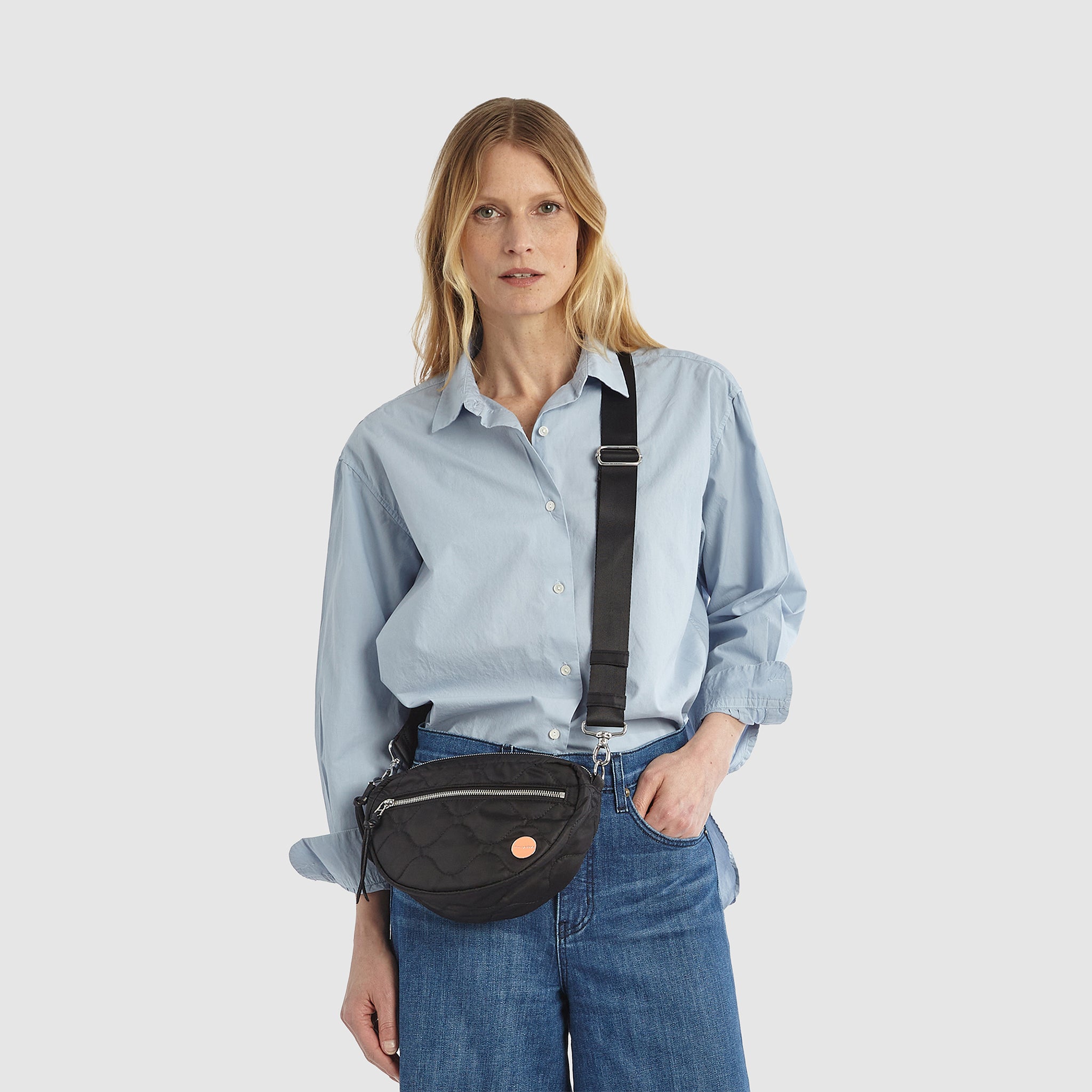 shortyLOVE small cruiser small crossbody bag in black; on model in blue button down shirt and jeans against white background.