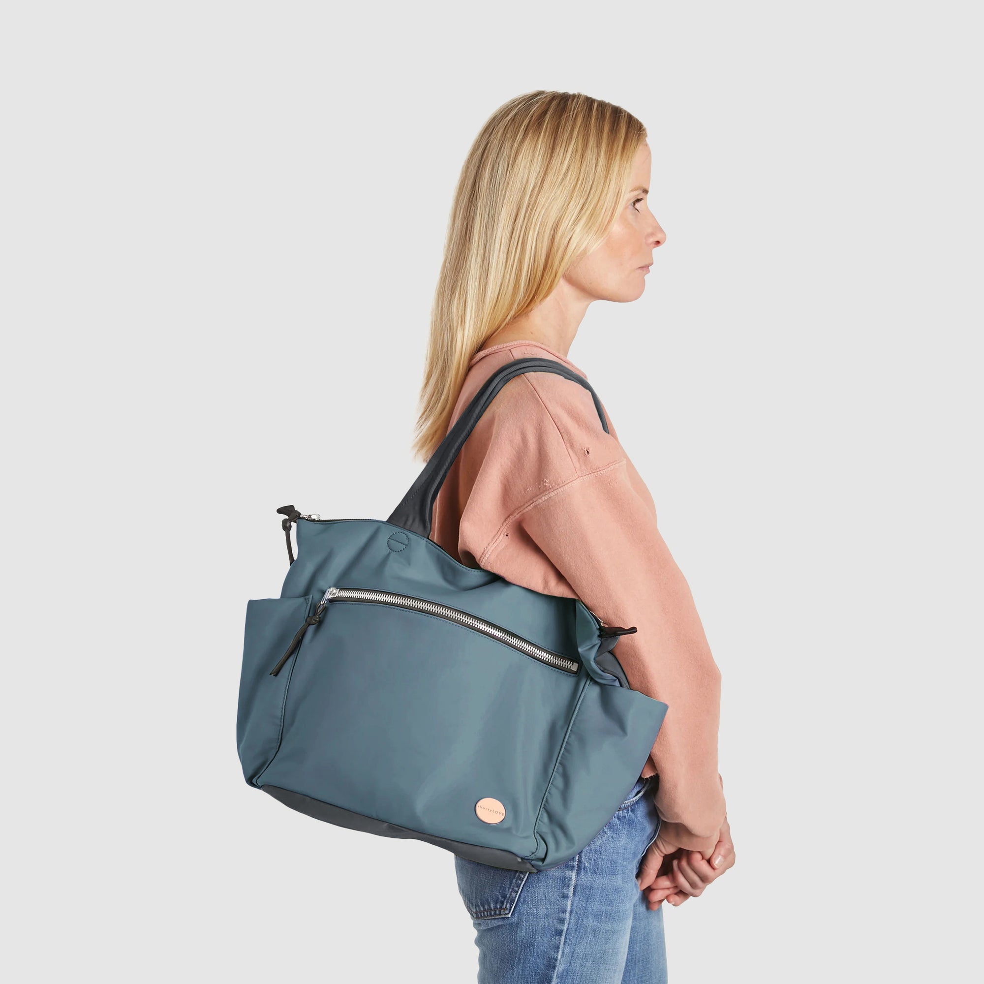 shortyLOVE tillie tote bag in steel blue/charcoal; on model in peach sweatshirt and jeans against white background.