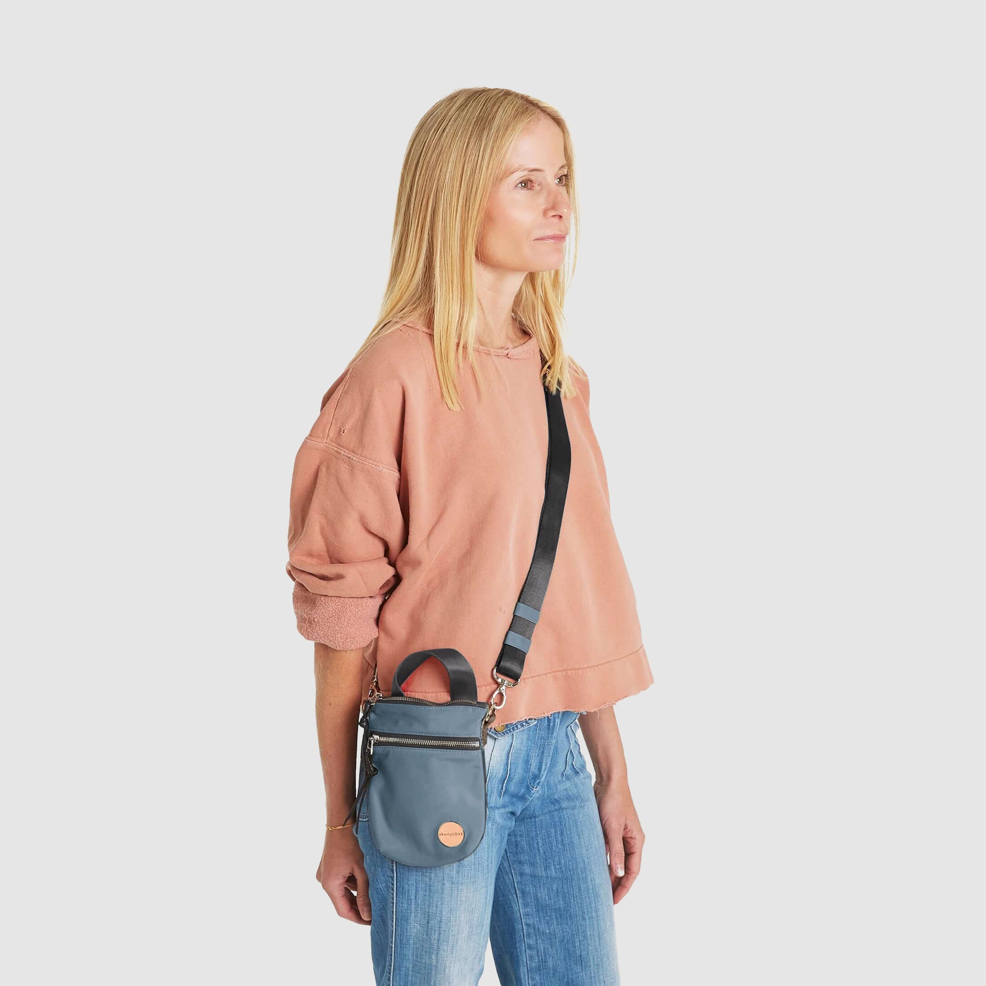 shortyLOVE shorthand small crossbody bag in steel blue/charcoal; on model in peach sweatshirt and jeans against white background.