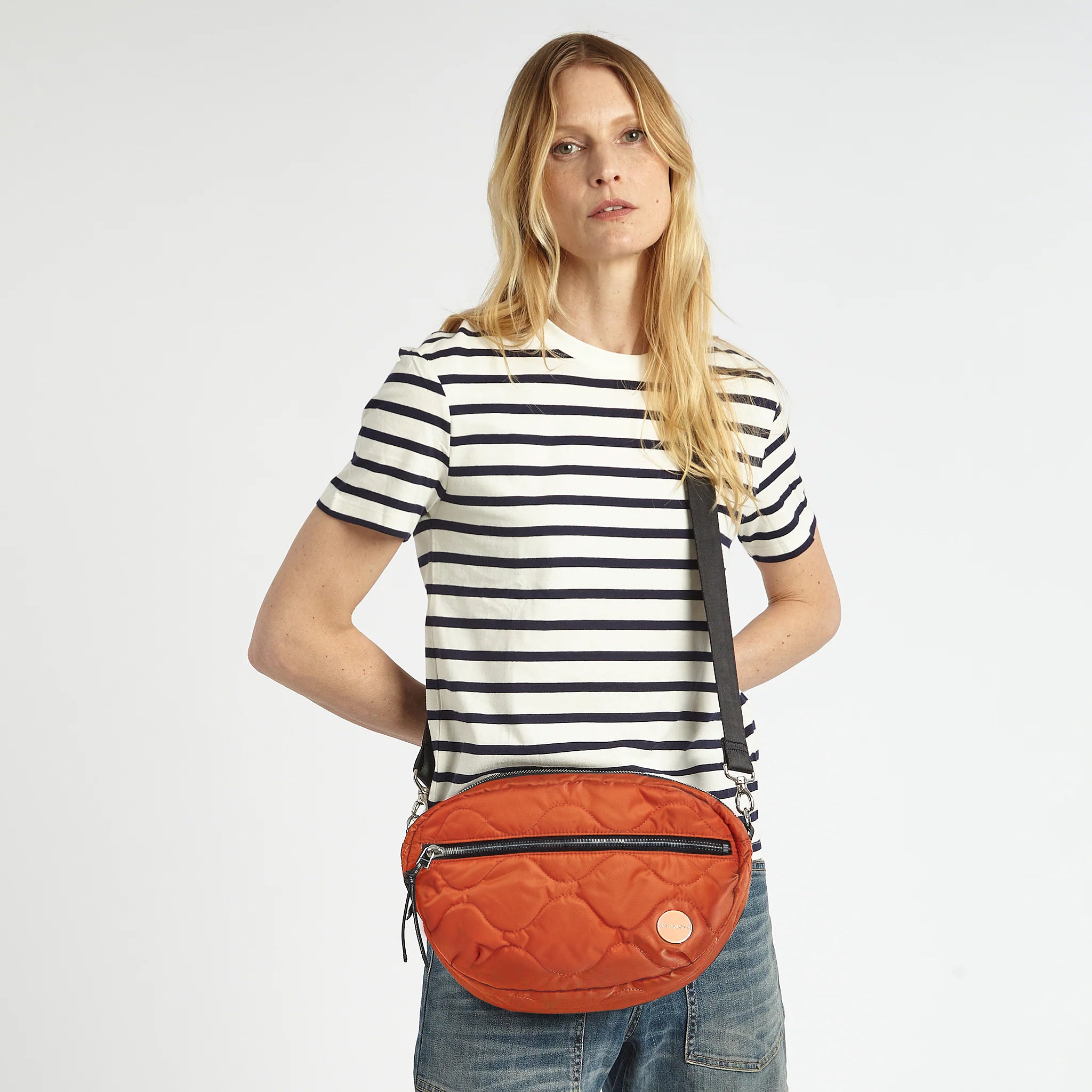 shortyLOVE cruiser medium crossbody bag in orange; on model in striped shirt and jeans against white background.