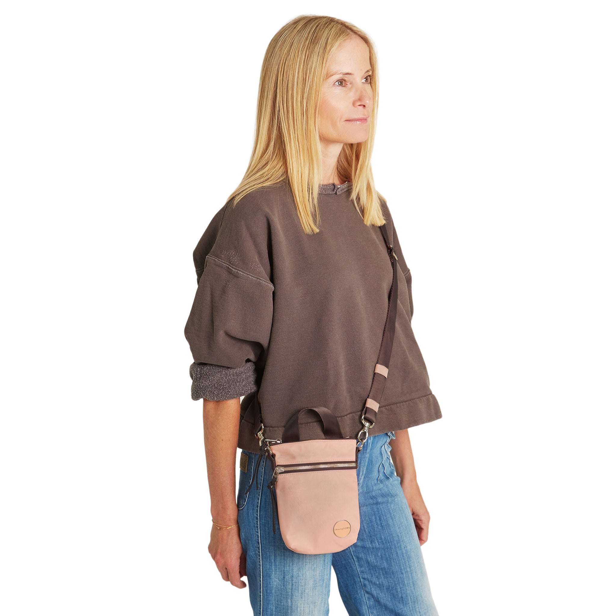 shortyLOVE shorthand small crossbody bag in dusty peach; on model in mocha sweatshirt and jeans against white background.