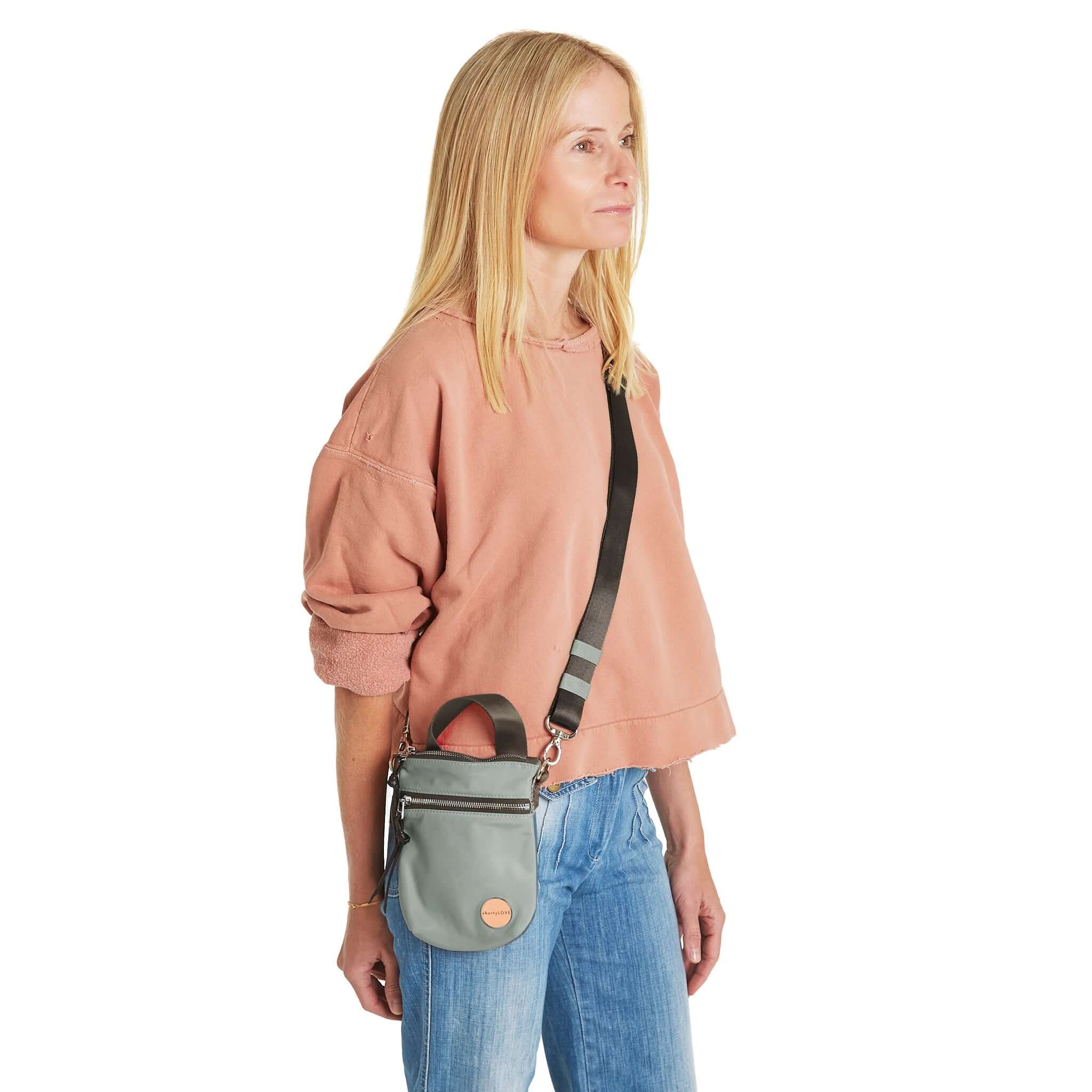 shortyLOVE shorthand small crossbody bag in slate/teal; on model in peach sweatshirt and jeans against white background.