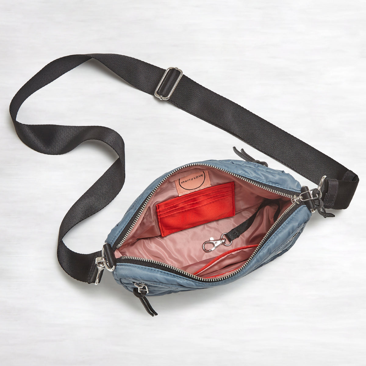 shortyLOVE small cruiser small crossbody bag in steel blue; top-down view showing interior blush lining against white background.