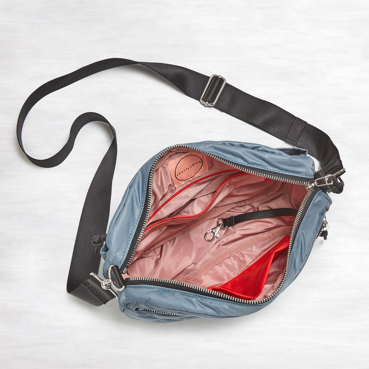 shortyLOVE cruiser medium crossbody bag in steel blue; top-down view showing interior blush lining against white background.
