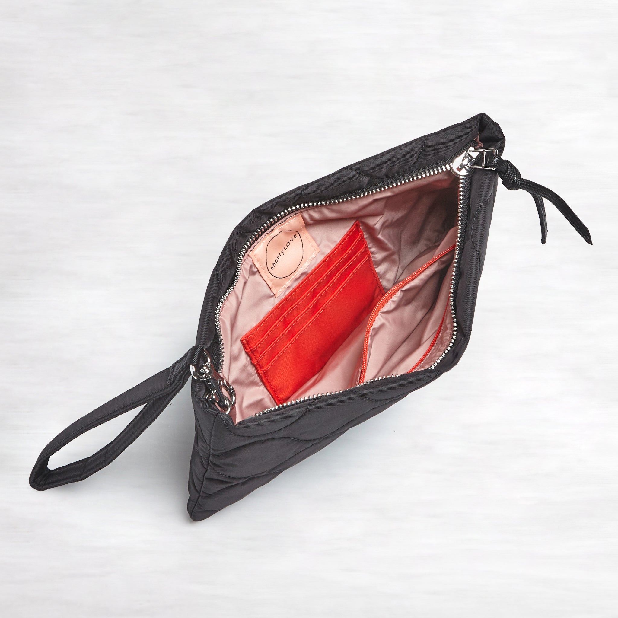 shortyLOVE cleo wristlet clutch in black; top-down view showing interior blush lining against white background.