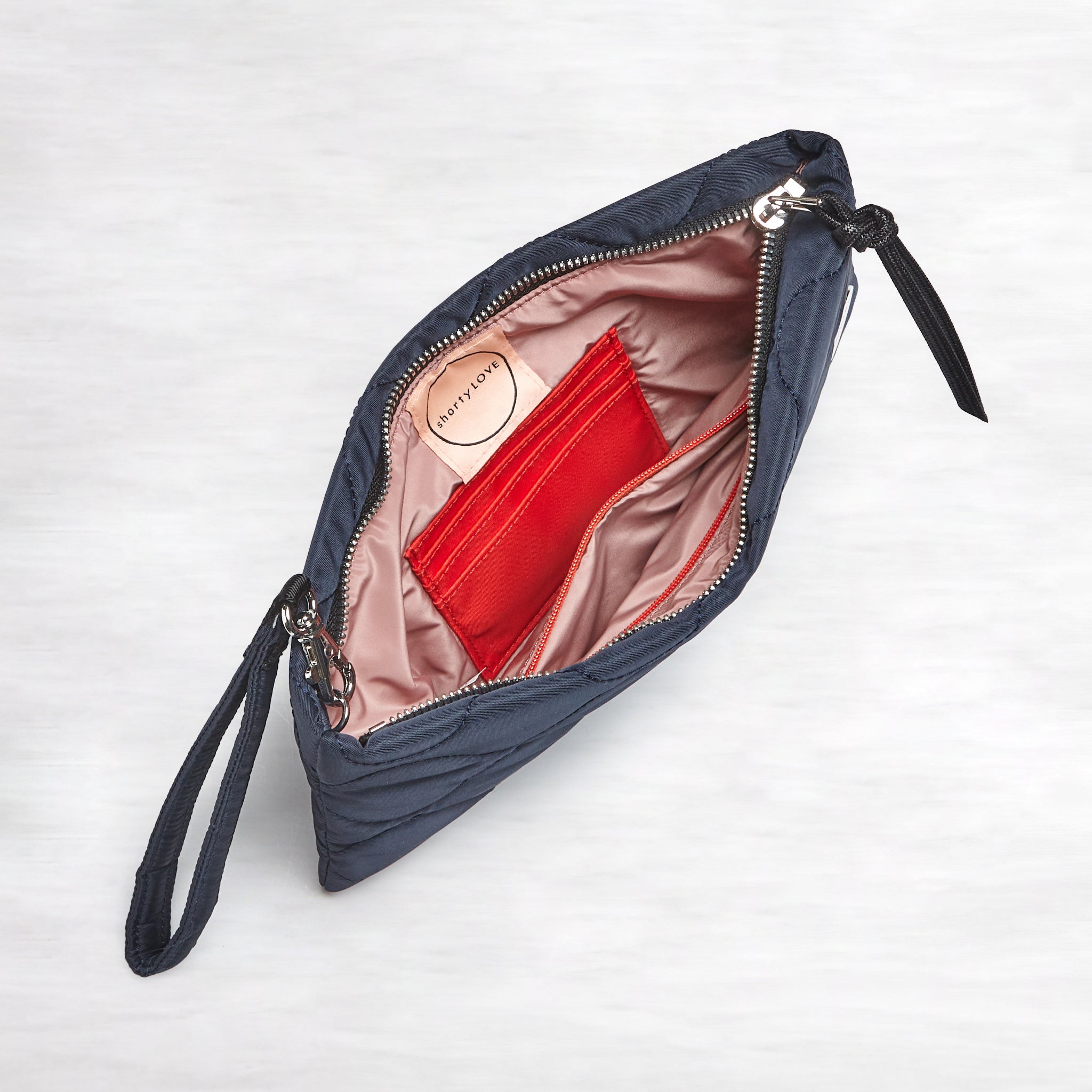 shortyLOVE cleo wristlet clutch in midnight; top-down view showing interior blush lining against white background.