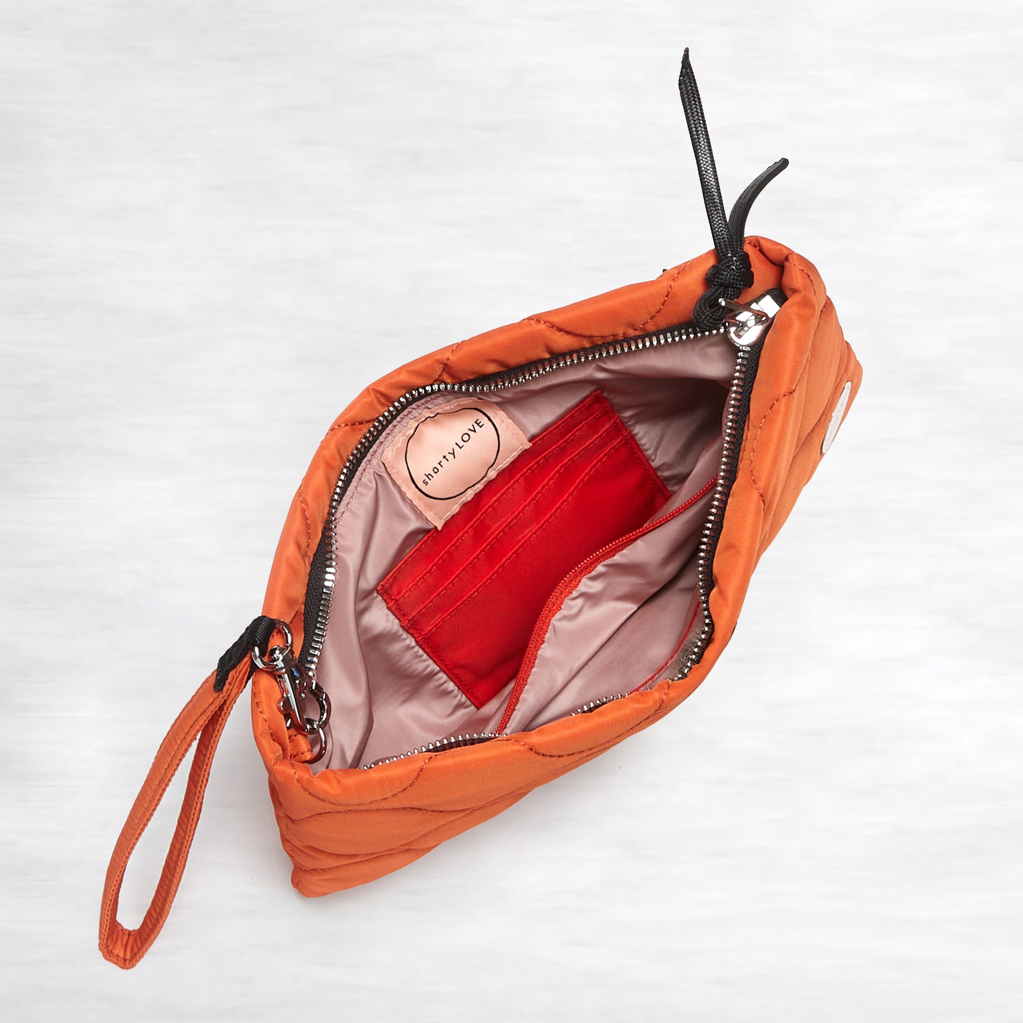 shortyLOVE cleo wristlet clutch in orange; top-down view showing interior blush lining against white background.