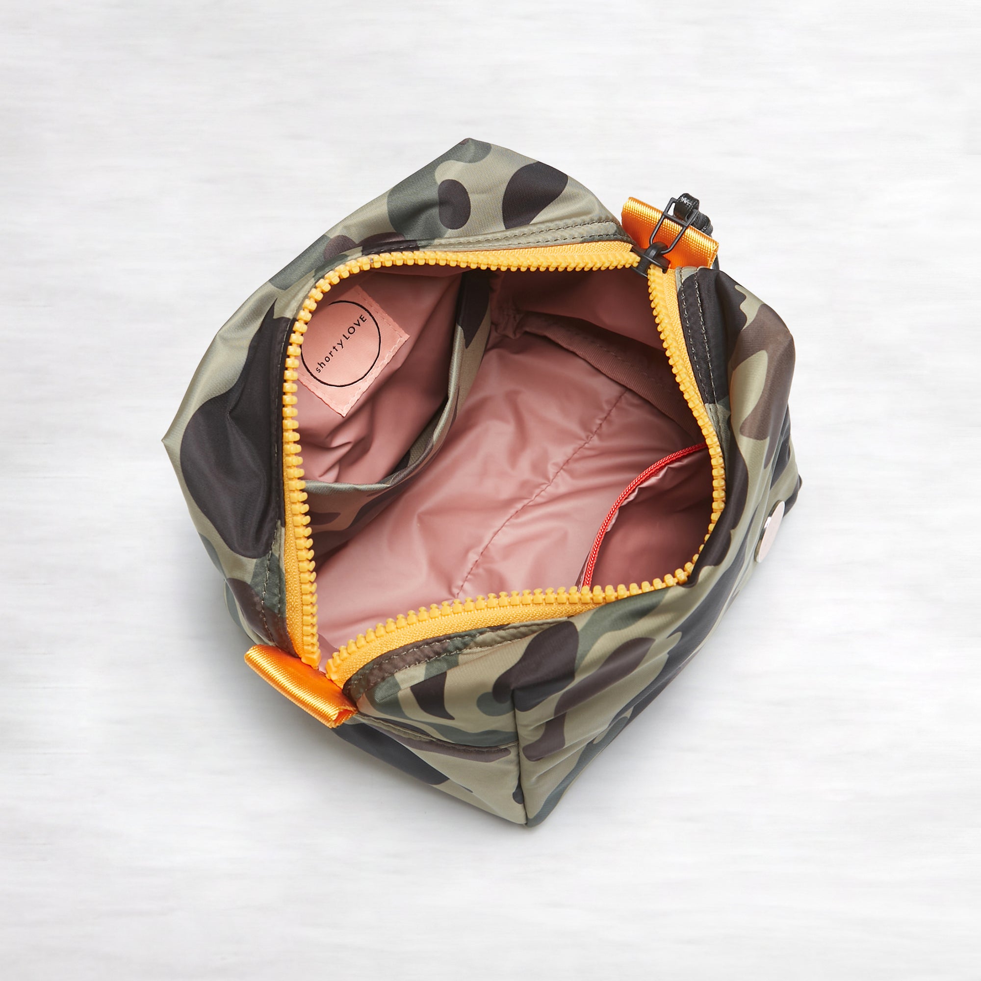 shortyLOVE stevie cosmetic bag in green camo; top-down view showing interior pink lining against white background.