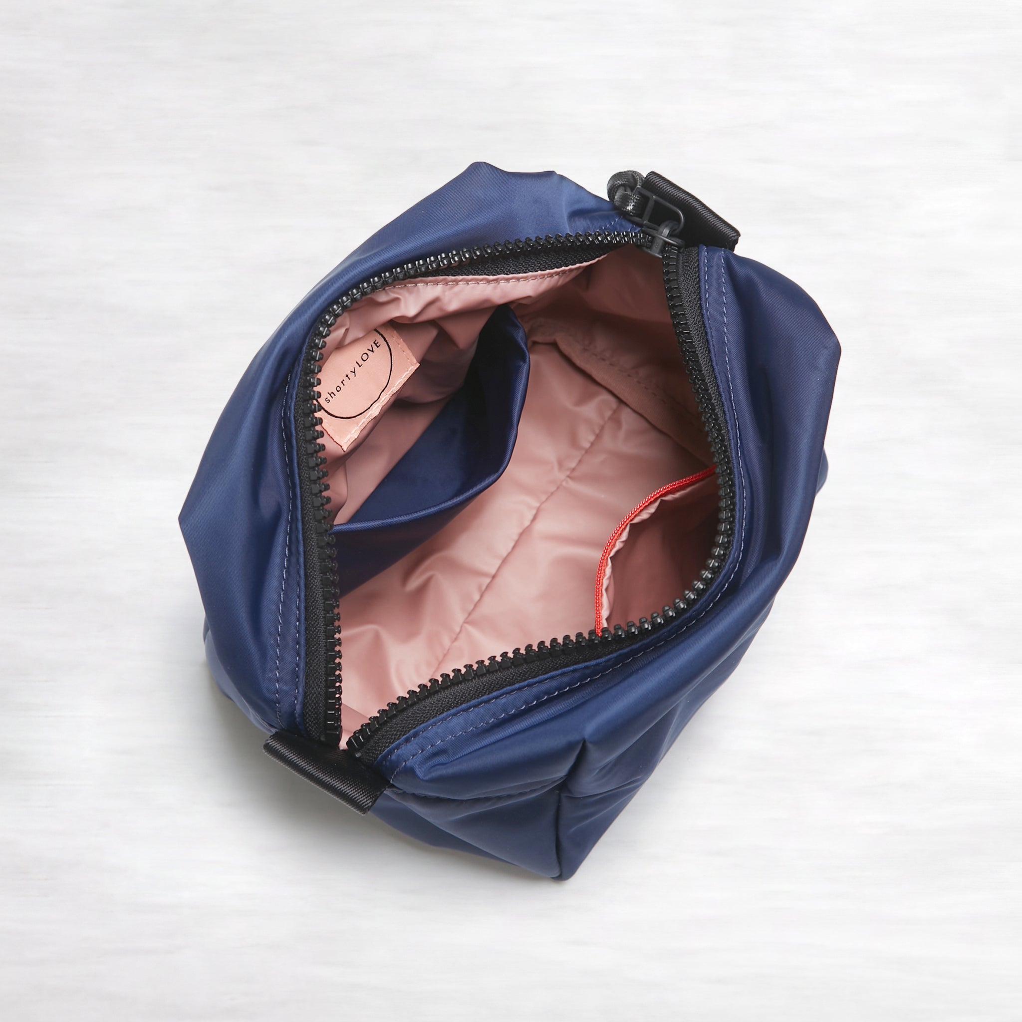 shortyLOVE stevie cosmetic bag in navy; top-down view showing interior pink lining against white background.
