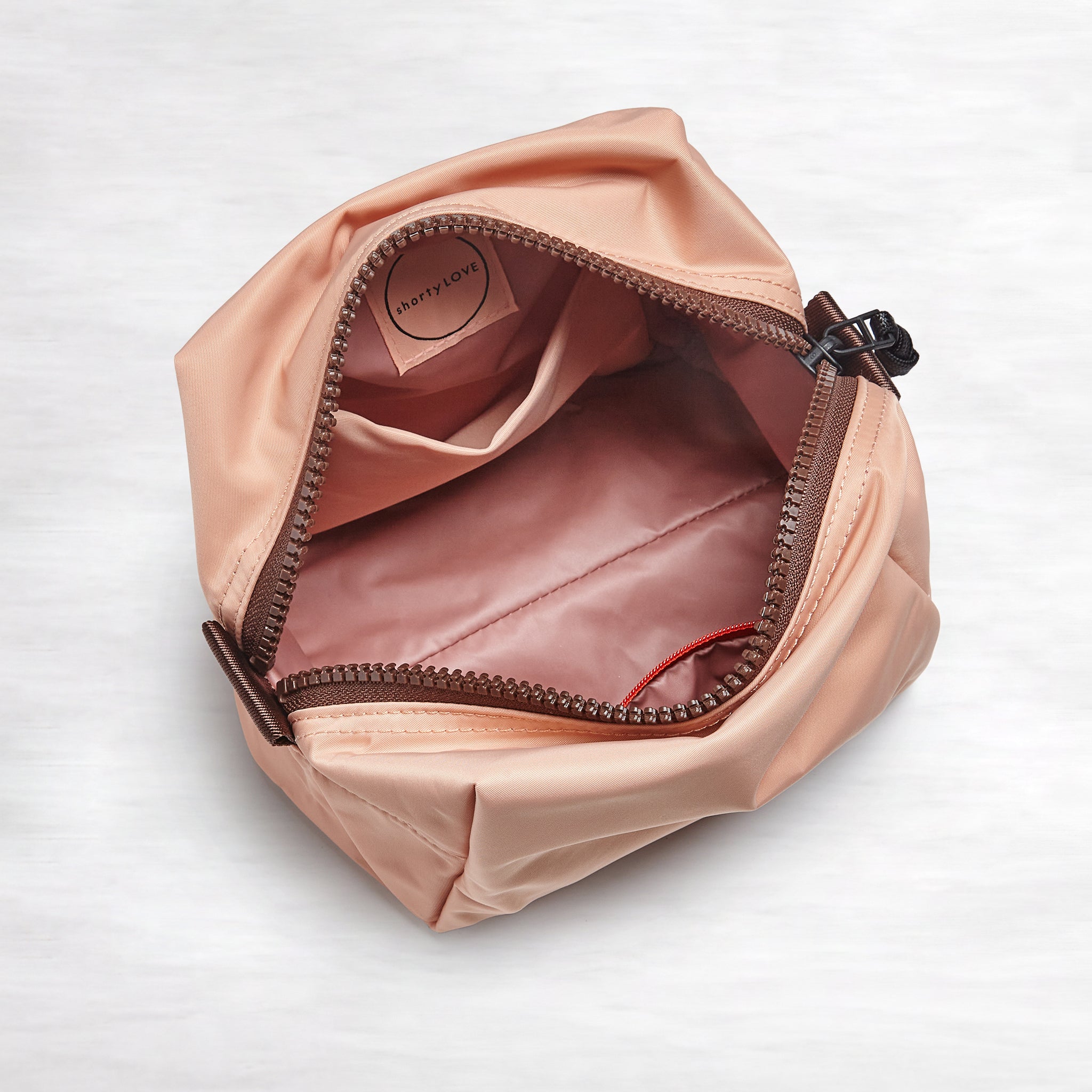 shortyLOVE stevie cosmetic bag in dusty peach; top-down view showing interior blush/red lining against white background.