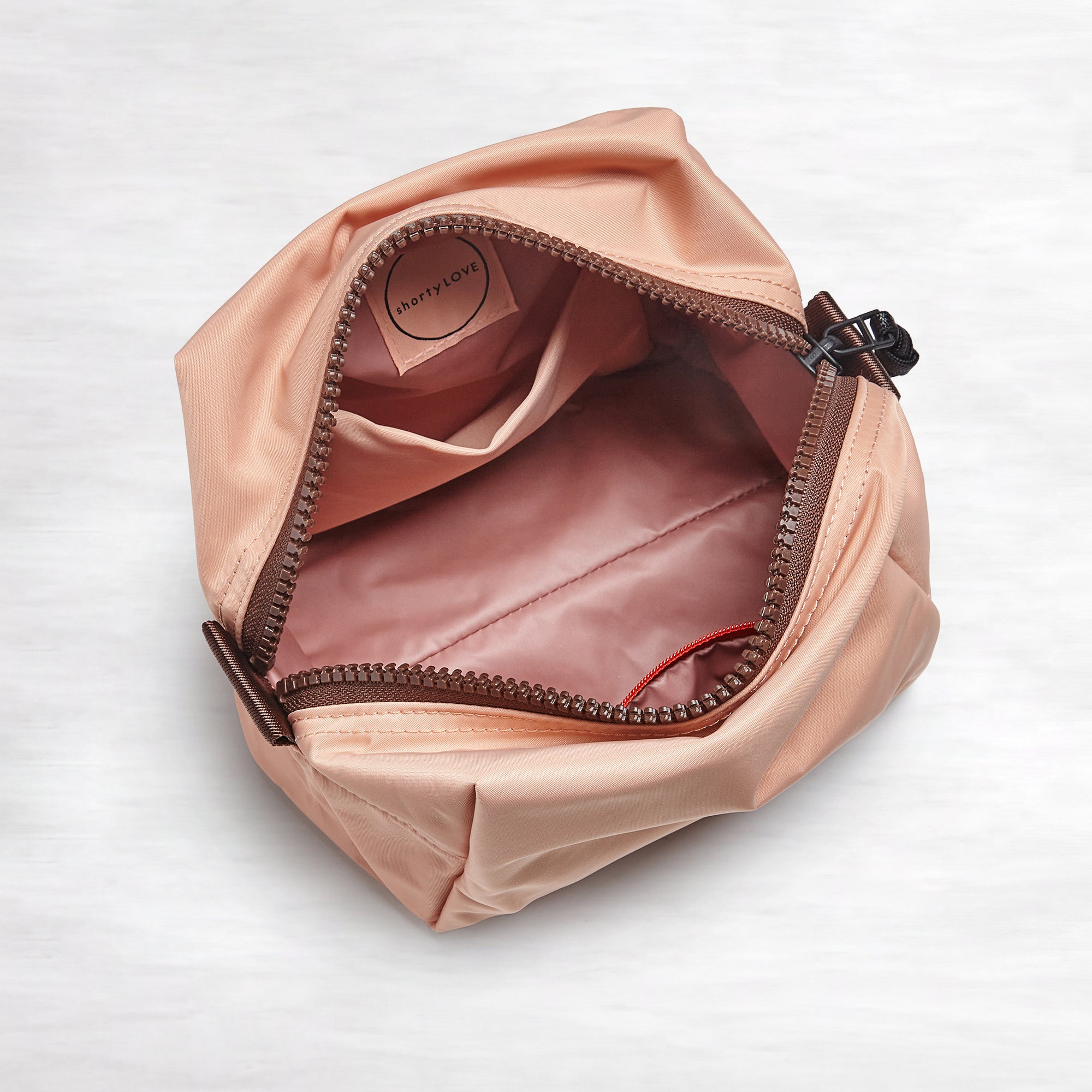 shortyLOVE stevie cosmetic bag in dusty peach; top-down view showing interior blush/red lining against white background.