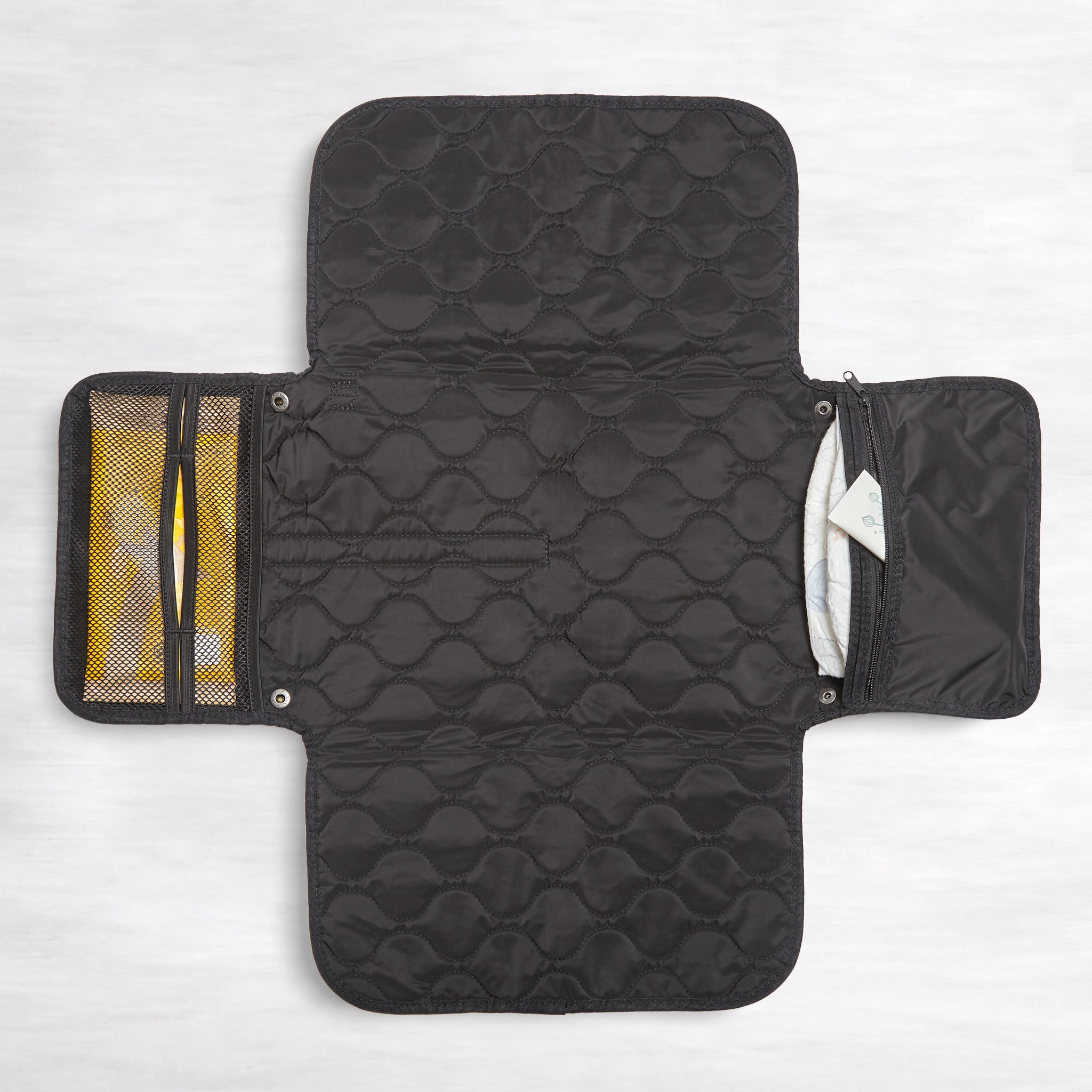 Black quilted diaper changing mat with multiple compartments on a white background