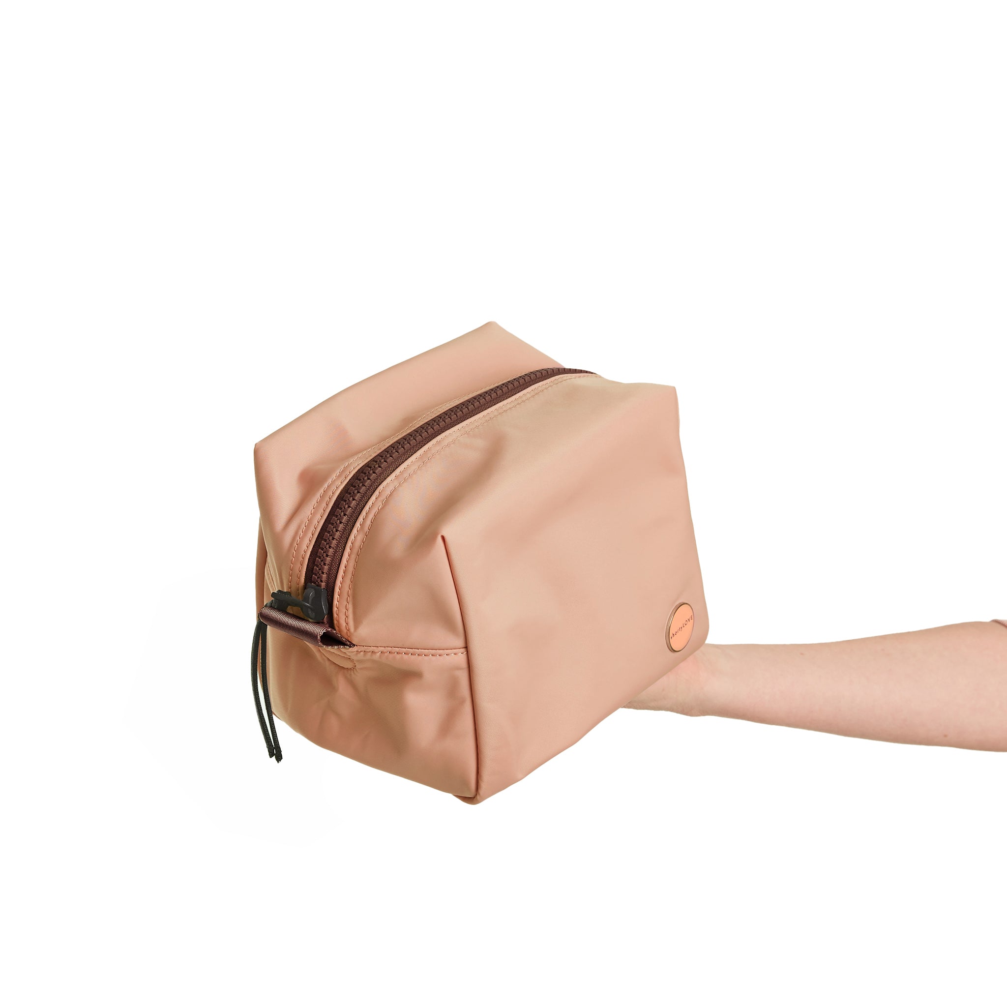 shortyLOVE stevie cosmetic bag in dusty peach; hand held by model against white background.