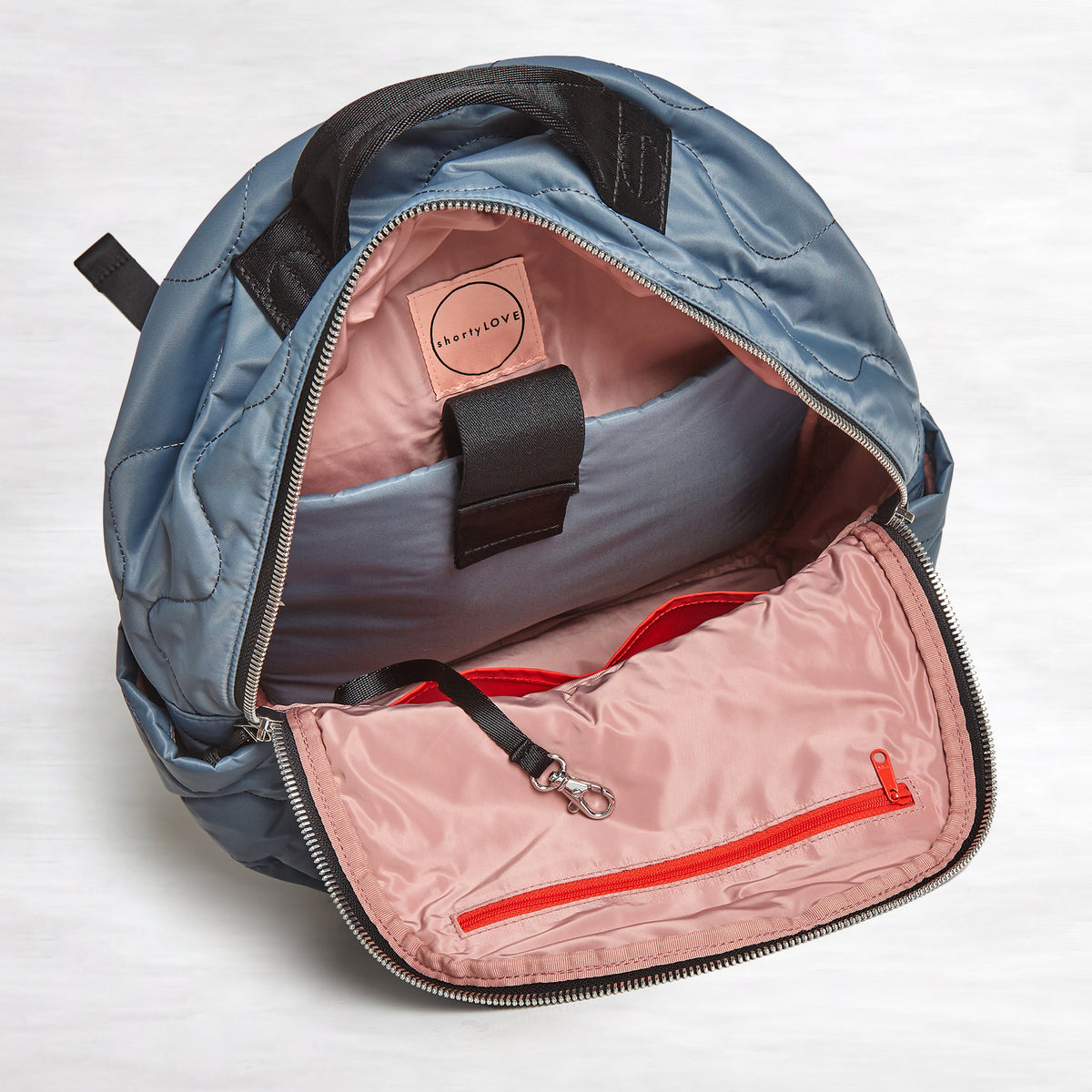 shortyLOVE tate backpack in steel blue; top-down view showing interior blush lining against white background.