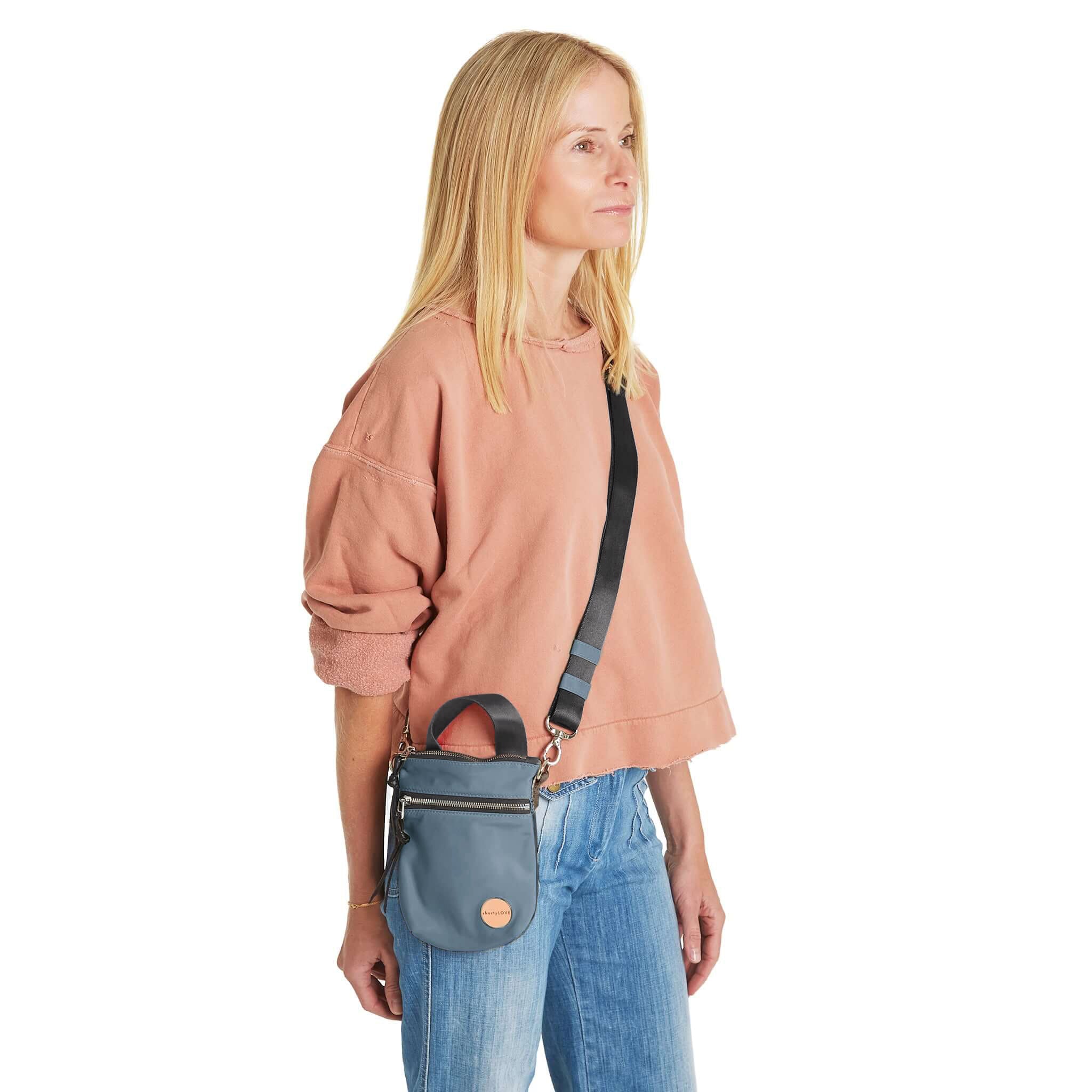 shortyLOVE shorthand small crossbody bag in steel blue/charcoal; on model in peach sweatshirt and jeans against white background.