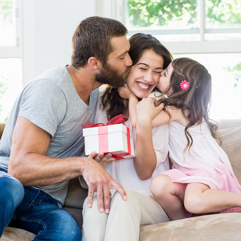 Family of three with a gift box on a couch in a bright room