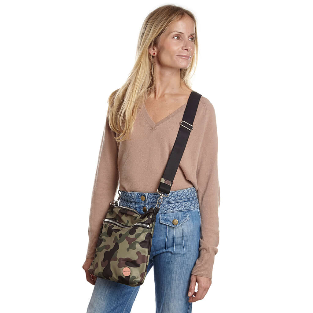 shortyLOVE amuse medium sized crossbody bag in green camo; on model in tan v-neck long sleeve sweater and jeans against white background.