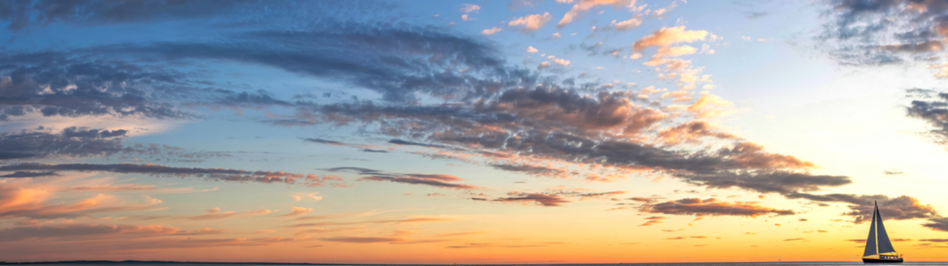 sailboat appears small against blue, pink and gold clouds at sunset
