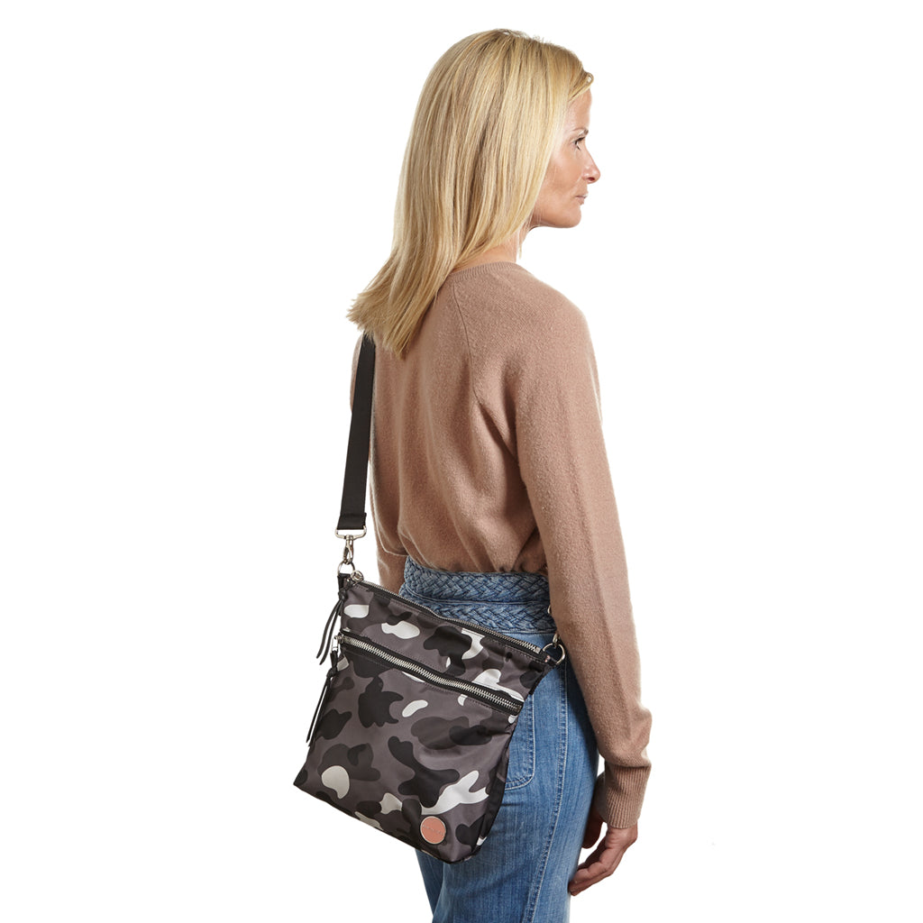 shortyLOVE amuse medium sized crossbody bag in grey camo; on model in blush rose top and jeans against white background.