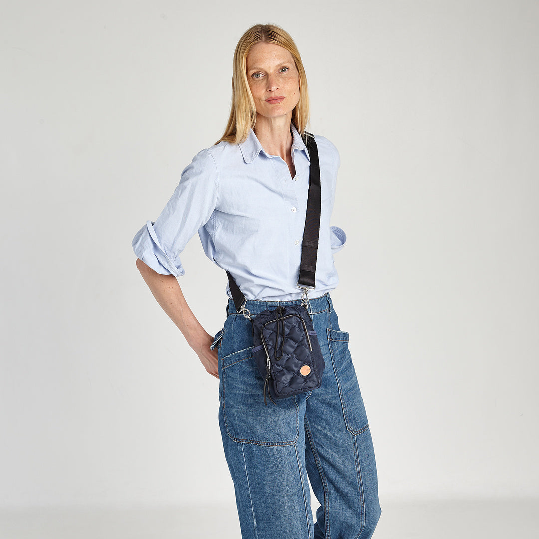 shortyLOVE bea sling bag in midnight; on model in blue top against grey background.