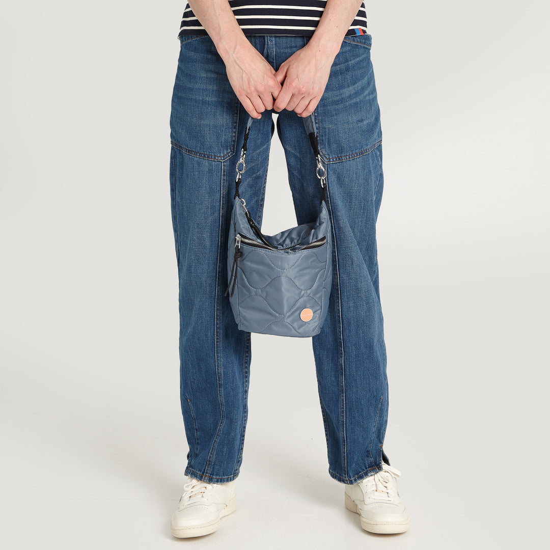 shortyLOVE marcel crossbody bucket bag in steel blue; on model in striped shirt and jeans against white background.