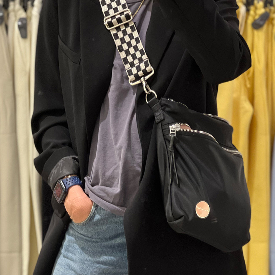 Person wearing a black coat with a checkered strap bag in a clothing store.