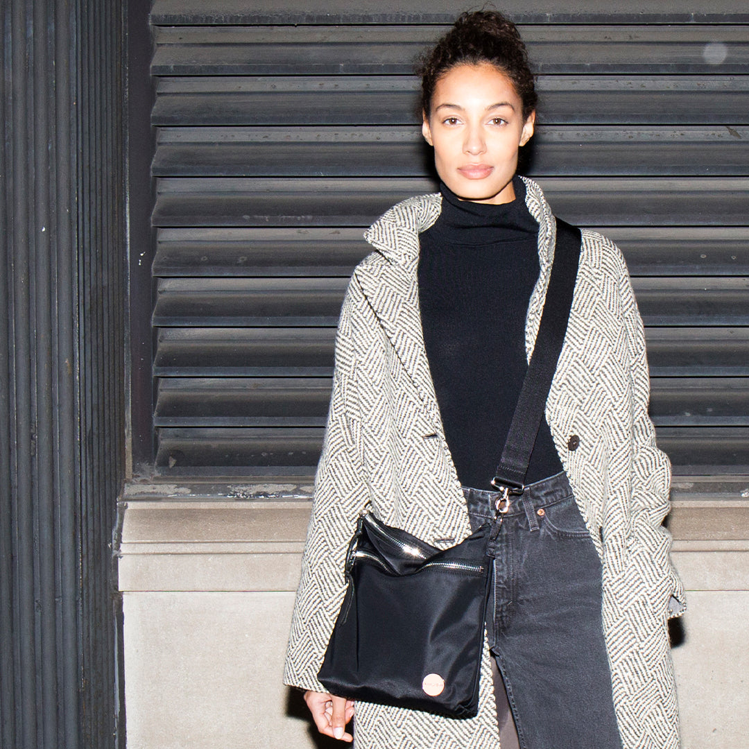 Person wearing a patterned coat and black amuse crossbody bag against a metallic shutter background