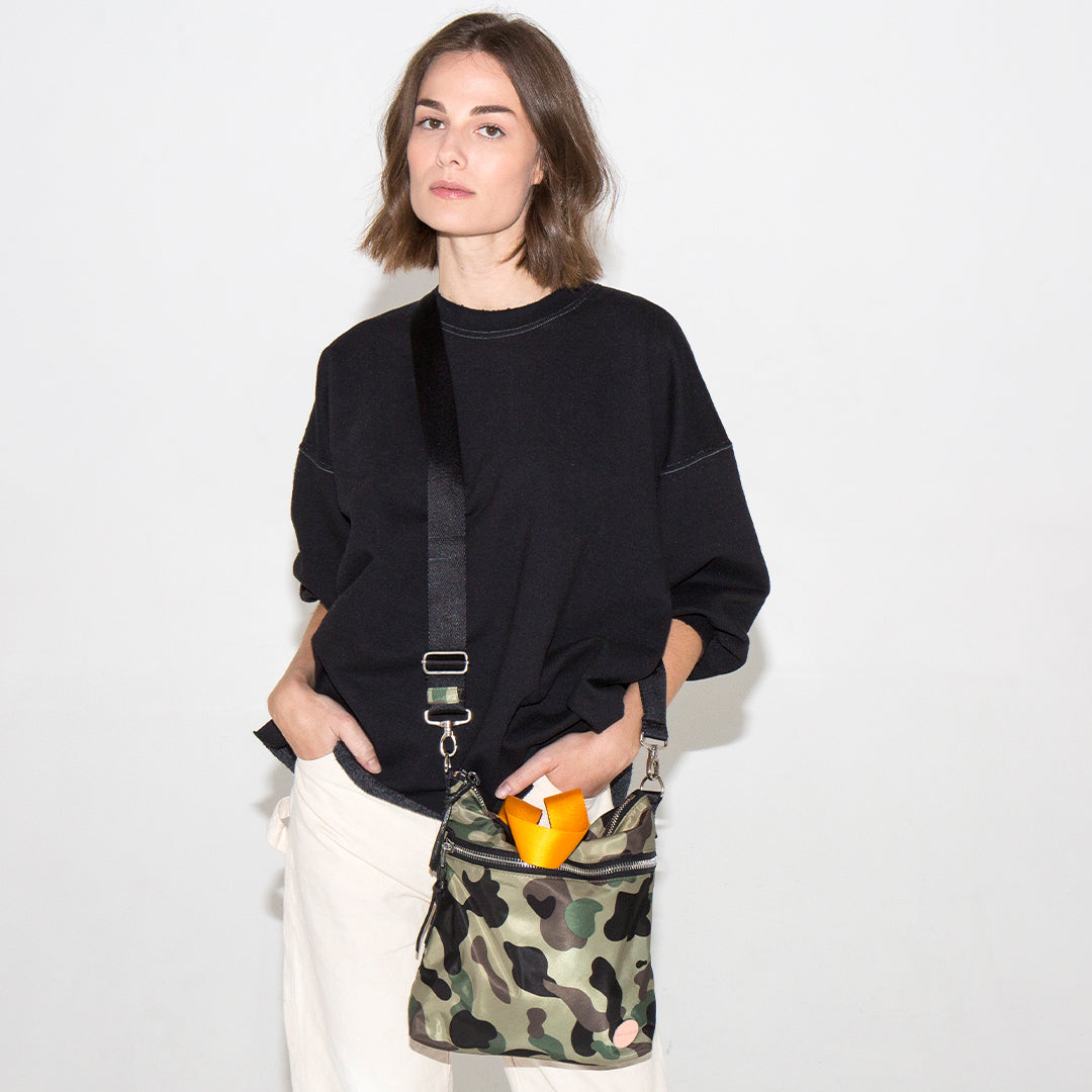 Woman holding a camouflage amuse crossbody bag with a white background