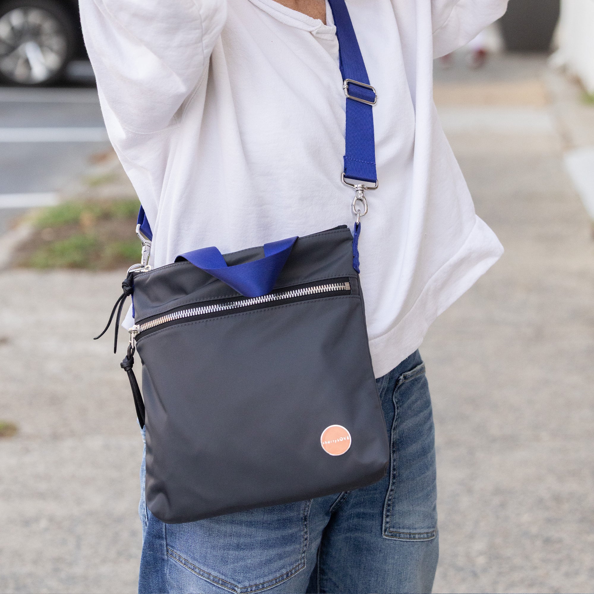 Person wearing a charcoal amuse crossbody bag with a blue strap on a street.