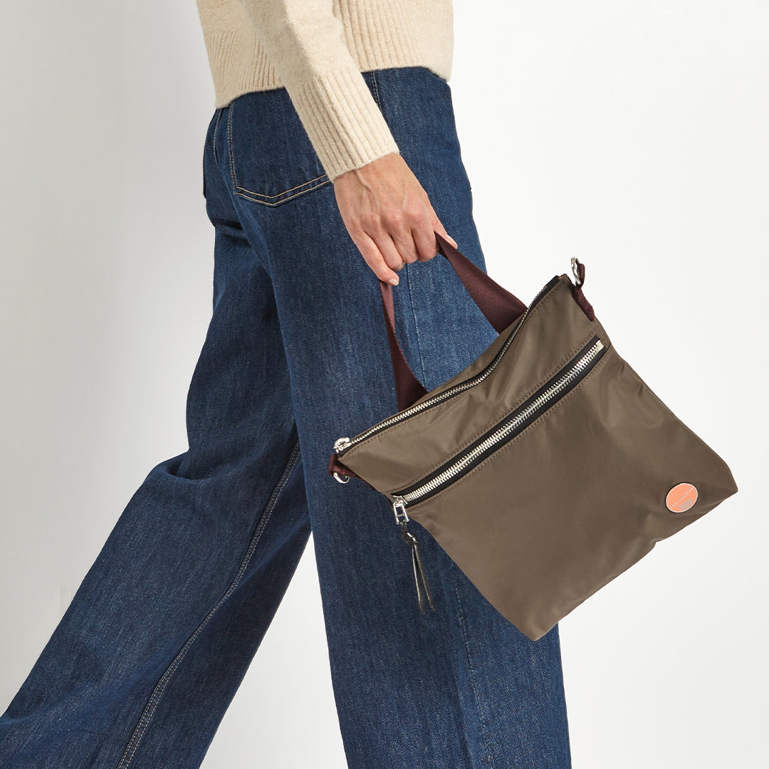 Person holding a mocha amuse crossbody bag with a burgundy accent on a plain background