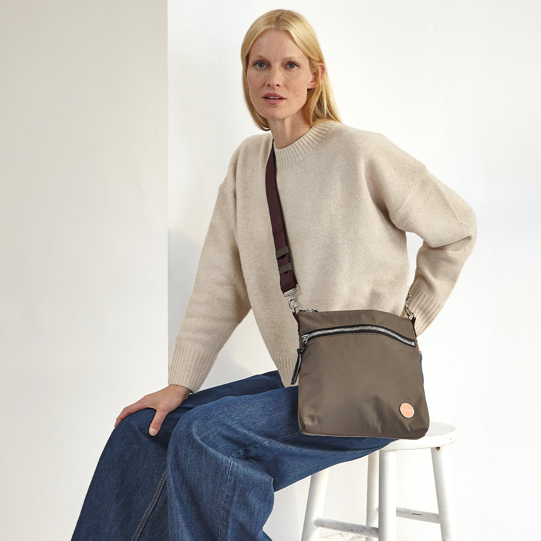 Woman holding a mocha amuse crossbody bag against a white background