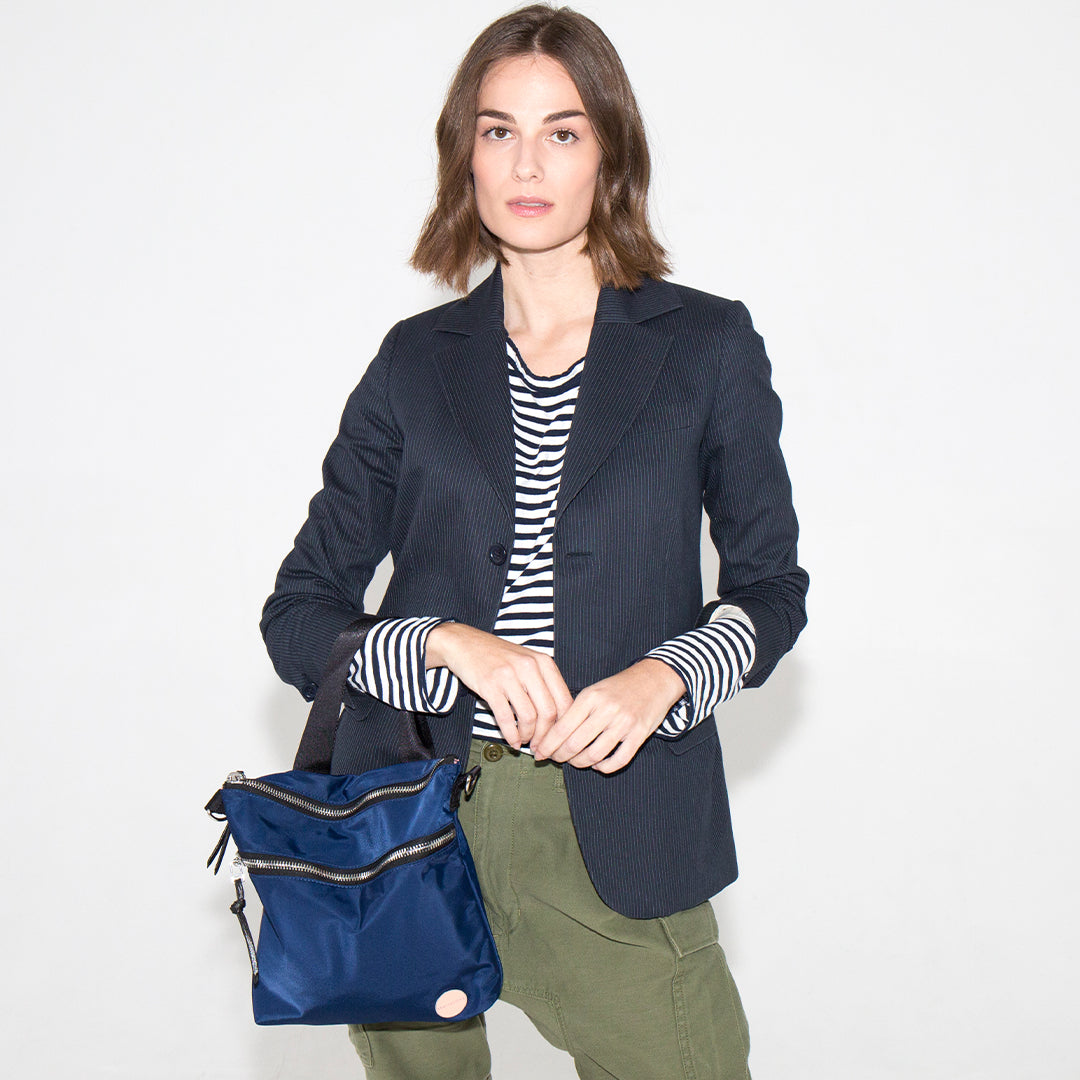 Woman holding a navy amuse crossbody bag against a white background