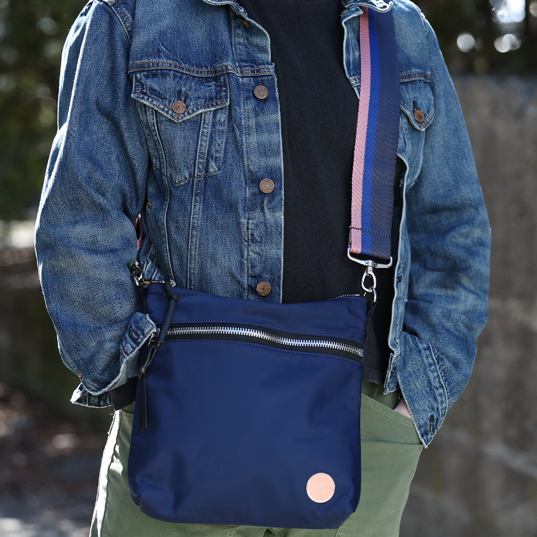 Person wearing a blue denim jacket with a navy blue bag over one shoulder outdoors.