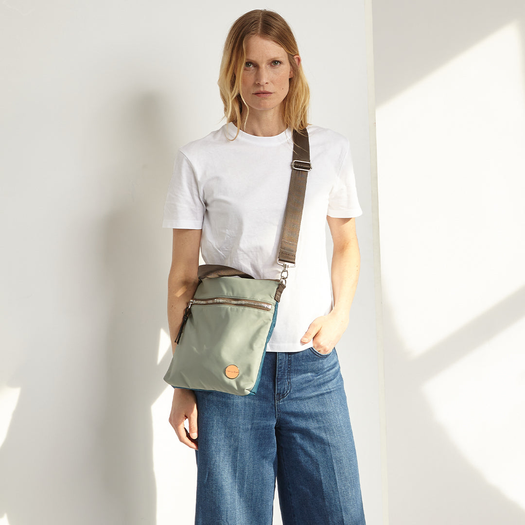 Person wearing a slate/teal amuse crossbody bag against a white background