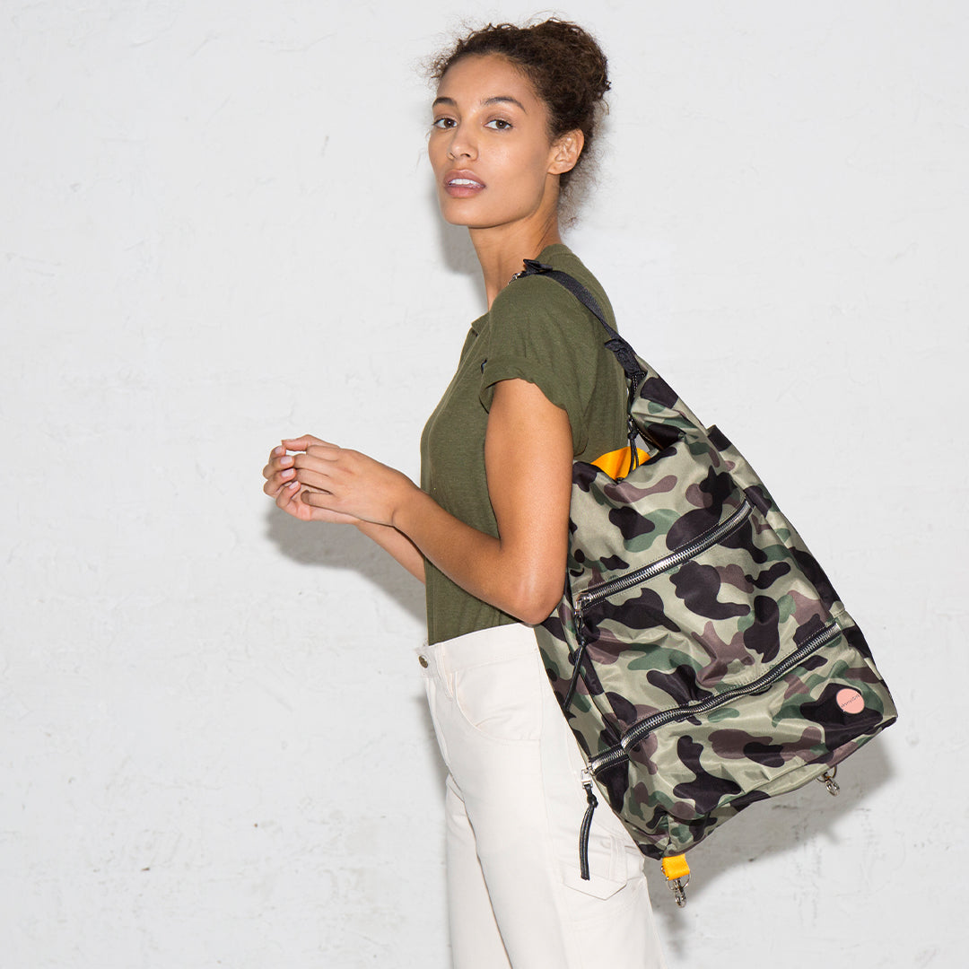 Woman wearing a green camo boxer backpack against a white background.